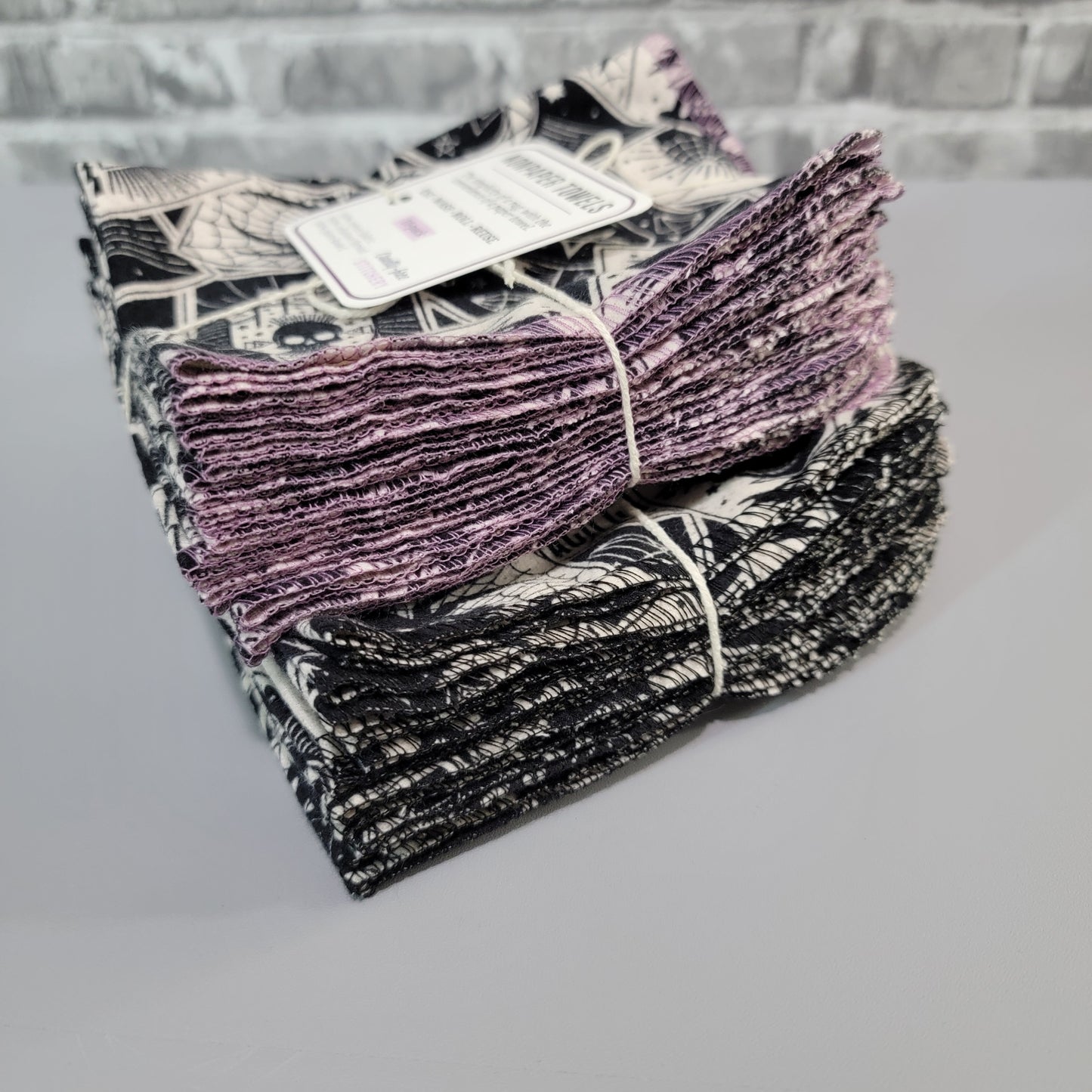 Two packs of the tarot cards NonPaper Towels stacked, one with the lilac purple stitching, and one with black stitching.