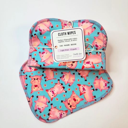 A bundled pack of the blue pigs reusable cloth wipes. They are folded in half and tied with a string and small tag. The shape of the wipes is a rounded rectangle, and stitched together with lilac purple thread.