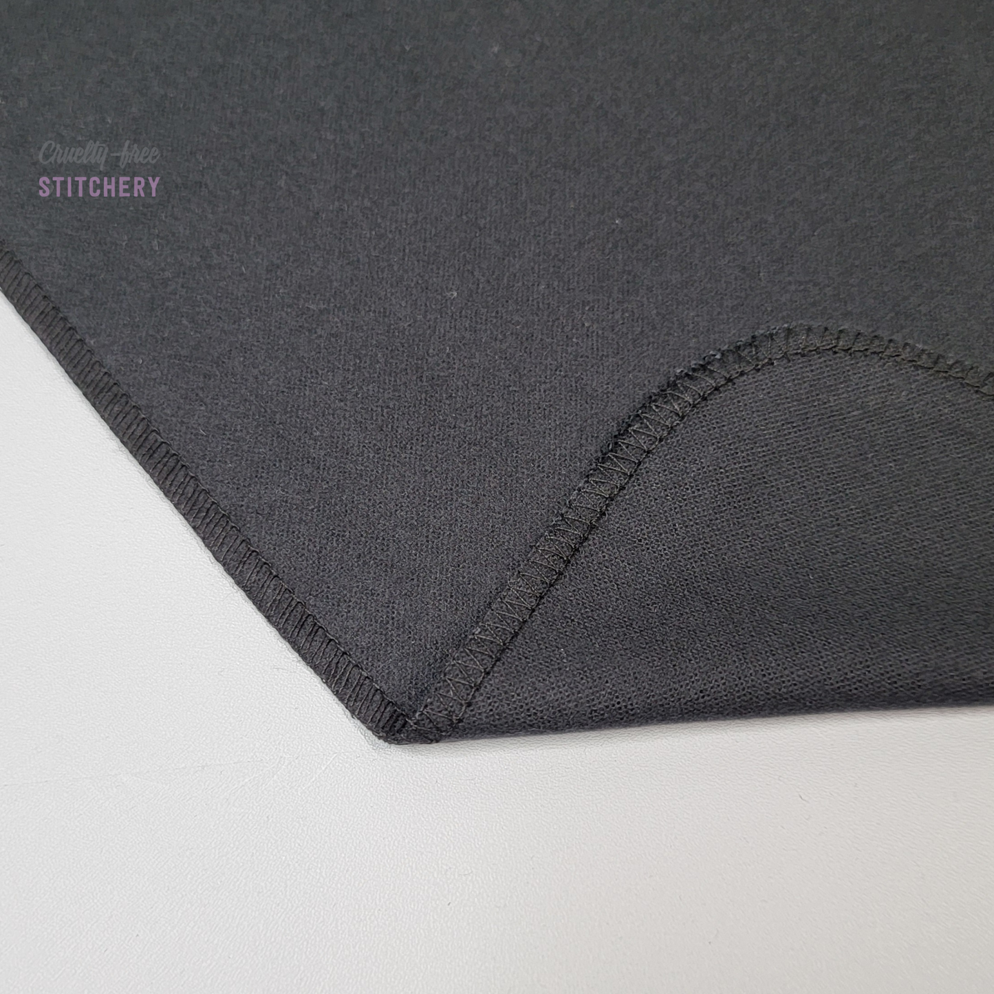A black NonPaper Towel with the corner folded up to show the stitching and that the back side is solid black. The stitching is black.
