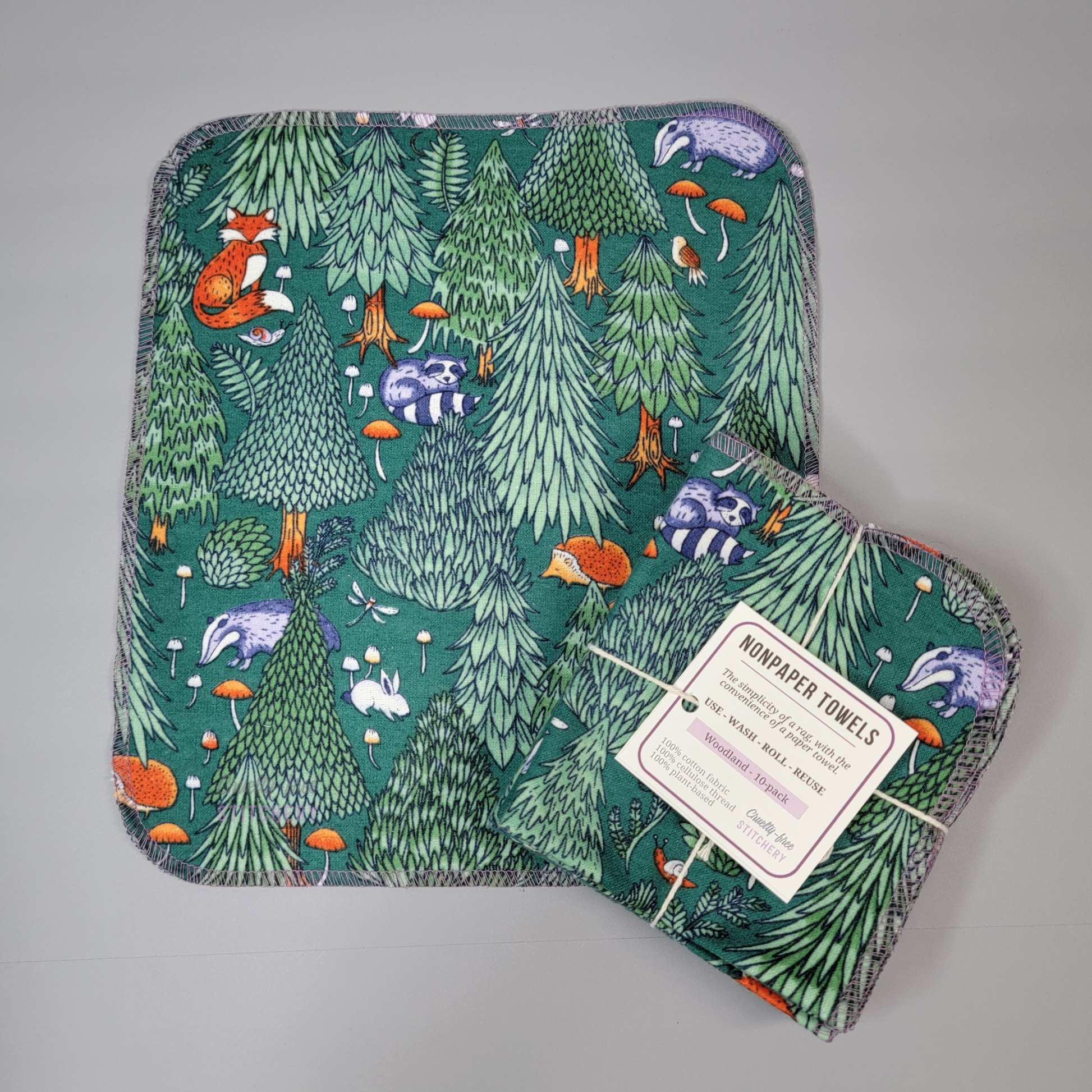 A woodland print NonPaper Towel laid flat next to a bundled pack. The bundle is tied with string and a tag like a gift.