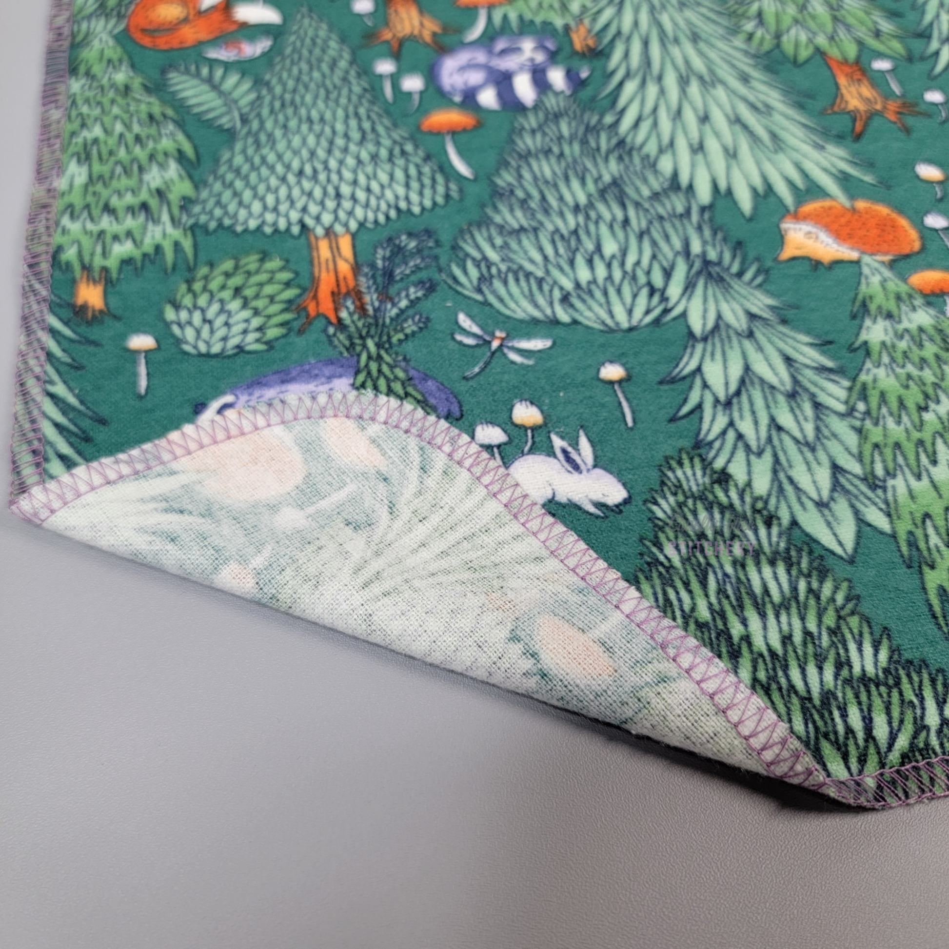 A woodland print NonPaper Towel with one corner folded up to show the stitching and the back side, which is unprinted.