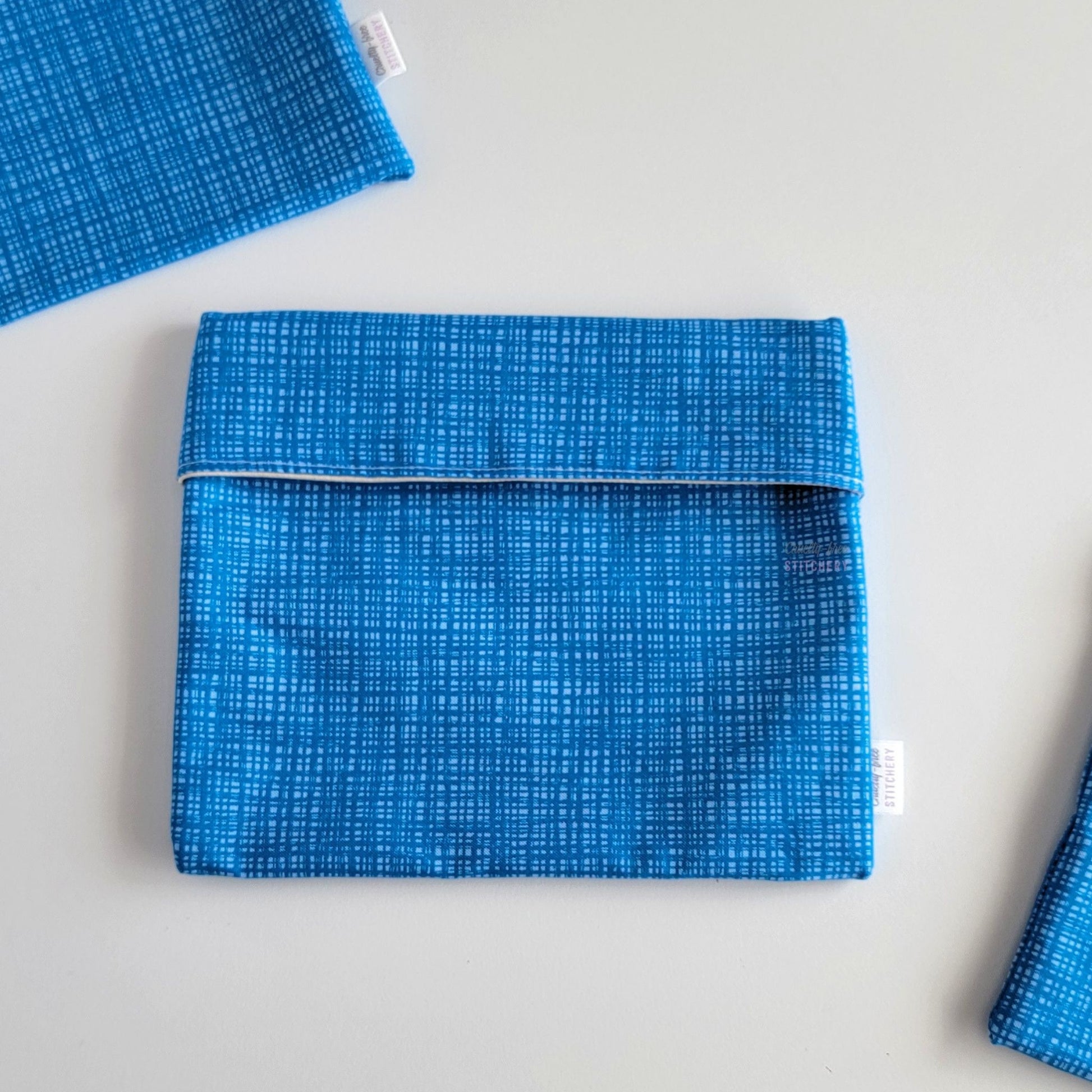 The Blue Texture Foldover Reusable Snack Bag, shown closed with two other bags barely visible on the edges of the photo. 
