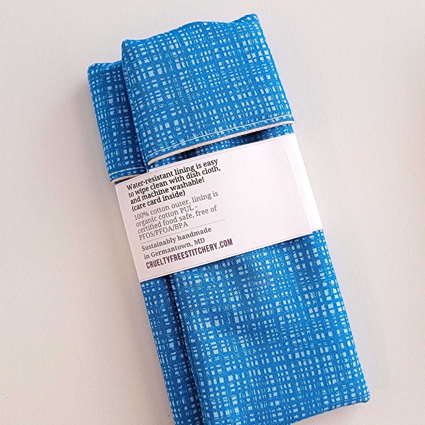 The back of the Snack Bag packaging. It says "Water resistant lining is easy to wipe clean with dish cloth, and machine washable. Care card inside. 100% cotton outer, lining is organic cotton PUL, cerfitied food-safe, free of PFOS, PFOA, BPA. Sustainable handmade in Germantown, MD" and our website url.