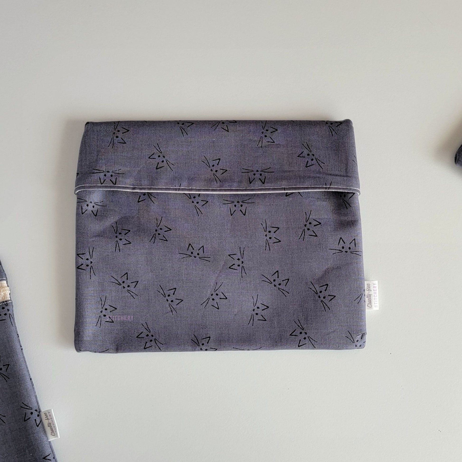 The Gray Cat Face Foldover Reusable Snack Bag, shown closed with two other bags barely visible on the edges of the photo. 
