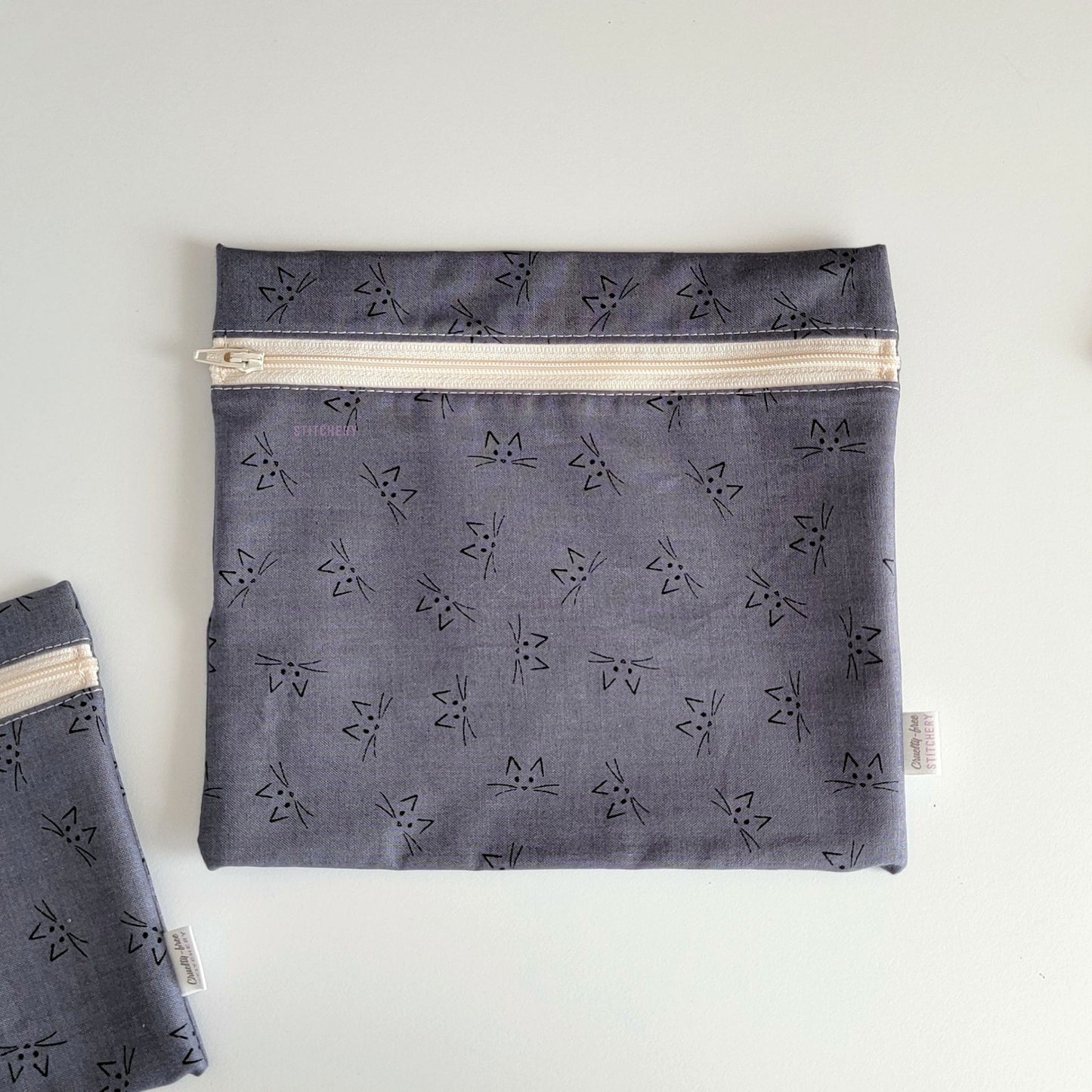 The Gray Cat Face Large Zip Reusable Snack Bag, shown closed with two other bags barely visible on the edges of the photo. 