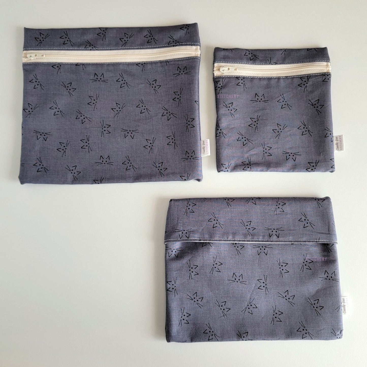Three Gray Cat Faces Reusable Snack Bags arranged separately to show the difference between sizes. Large Zip is not quite double the size of the Small Zip, and the Foldover is slightly smaller than the Large Zip.