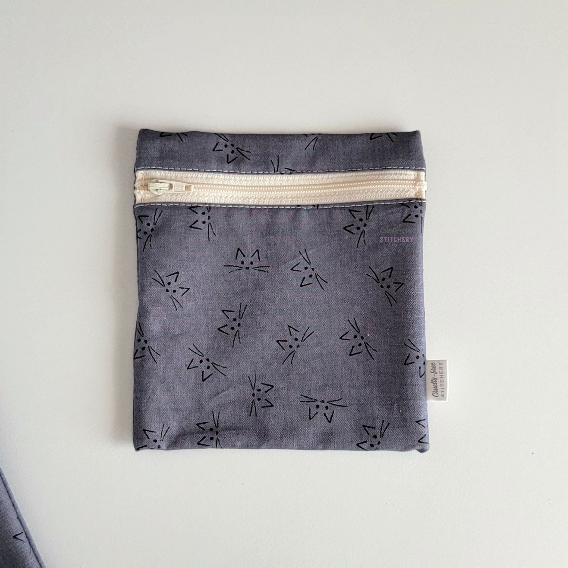 The Gray Cat Face Small Zip Reusable Snack Bag, shown closed with two other bags barely visible on the edges of the photo. 
