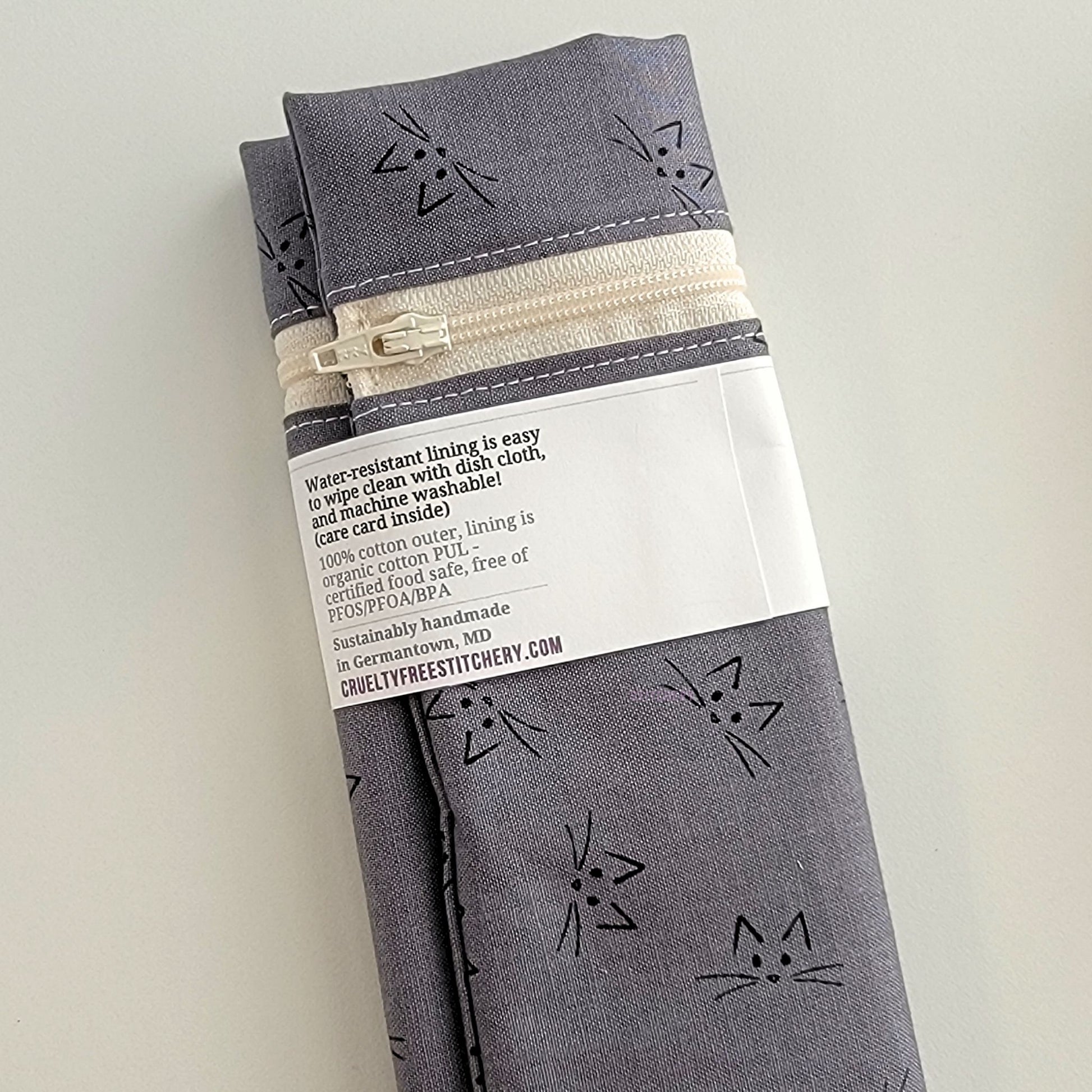 The back of the Snack Bag packaging. It says "Water resistant lining is easy to wipe clean with dish cloth, and machine washable. Care card inside. 100% cotton outer, lining is organic cotton PUL, cerfitied food-safe, free of PFOS, PFOA, BPA. Sustainable handmade in Germantown, MD" and our website url.