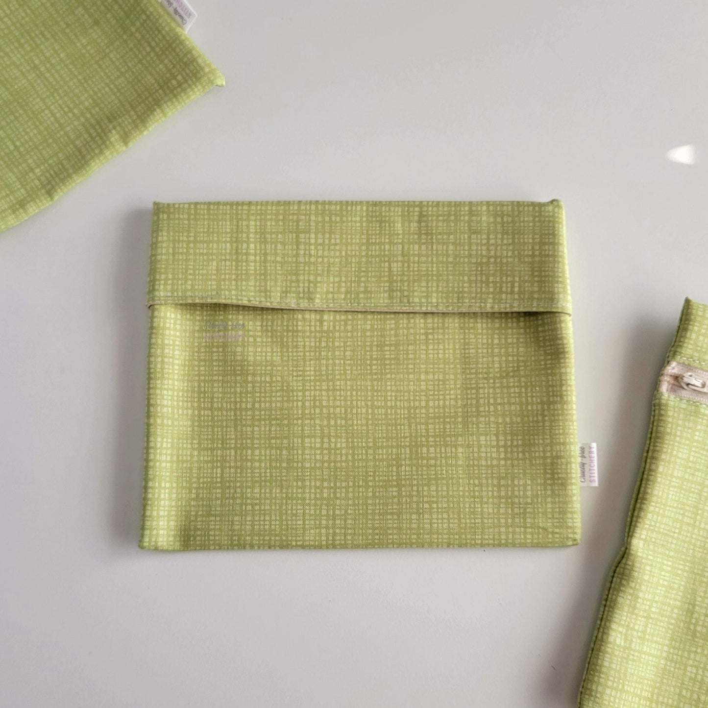 The light green texture Foldover Reusable Snack Bag, shown closed with two other bags barely visible on the edges of the photo. 