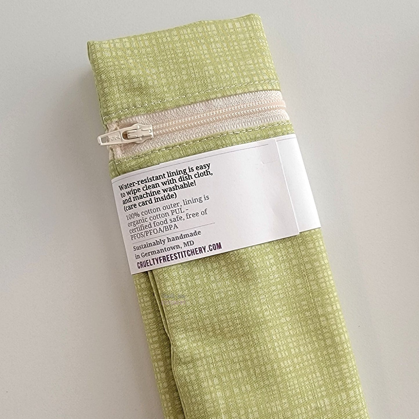 The back of the Snack Bag packaging. It says "Water resistant lining is easy to wipe clean with dish cloth, and machine washable. Care card inside. 100% cotton outer, lining is organic cotton PUL, cerfitied food-safe, free of PFOS, PFOA, BPA. Sustainable handmade in Germantown, MD" and our website url.
