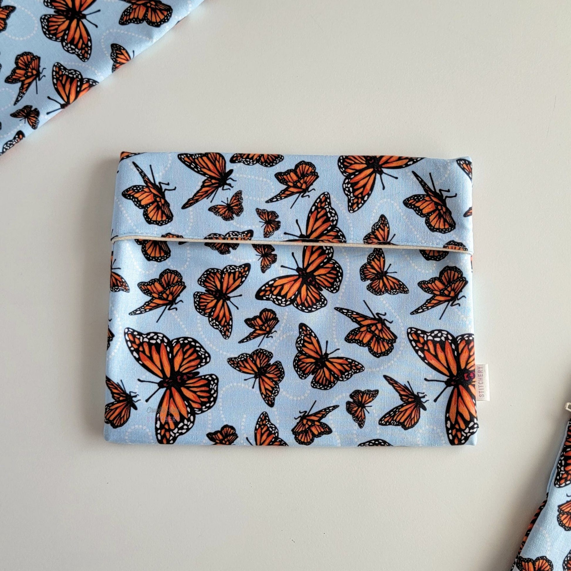 The Monarch Blue Foldover Reusable Snack Bag, shown closed with two other bags barely visible on the edges of the photo. 