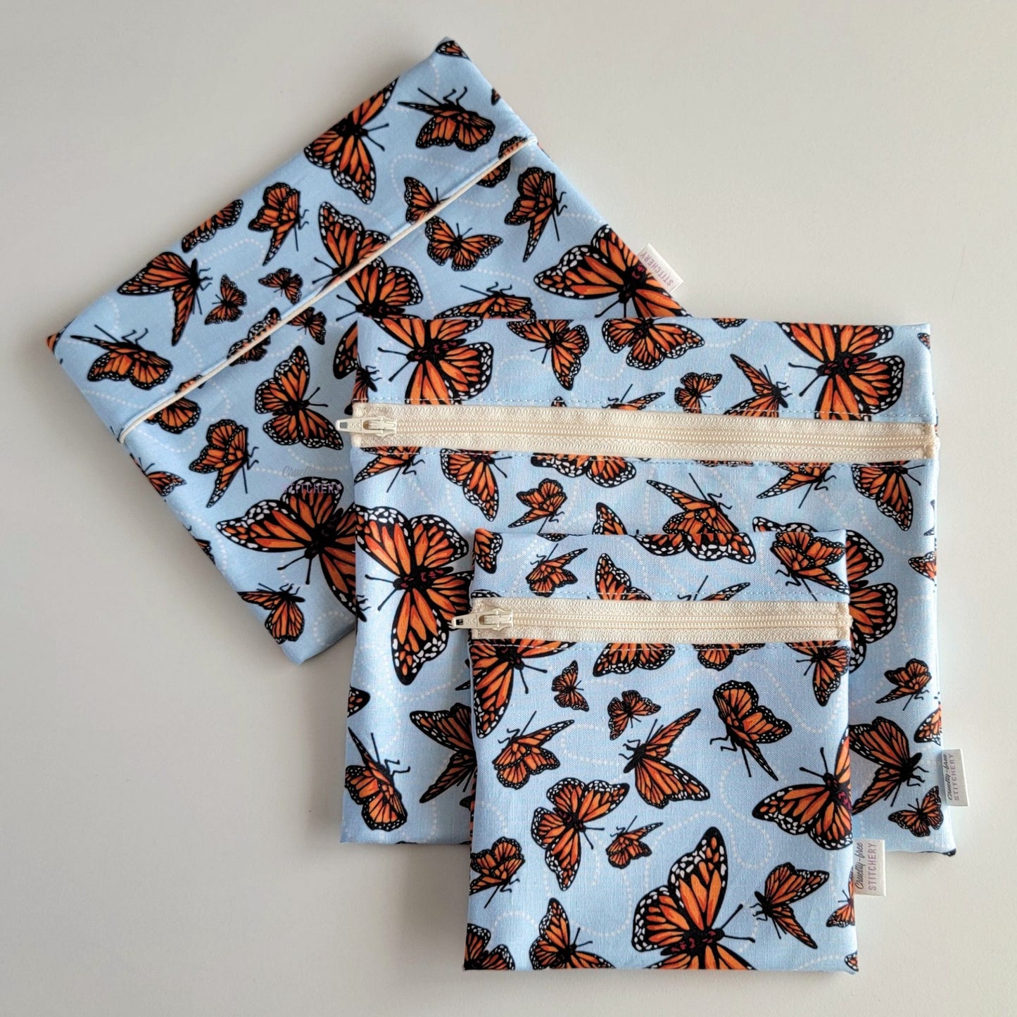 Set of three reusable snack bags with a monarch butterfly print, shown with the foldover style bag closed and behind the zipper styles.