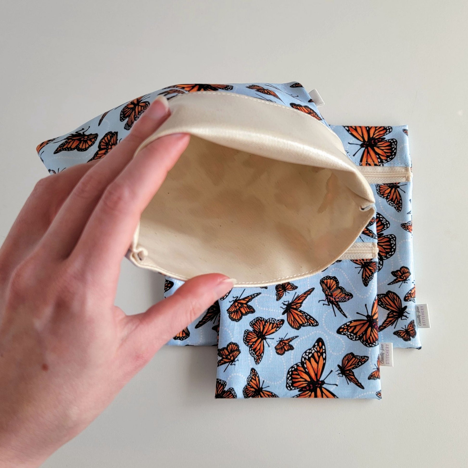 Hand holding a Monarch Blue Foldover Reusable Snack Bag open to show the lining inside, which is beige and is slightly shiny because it is water-resistant.