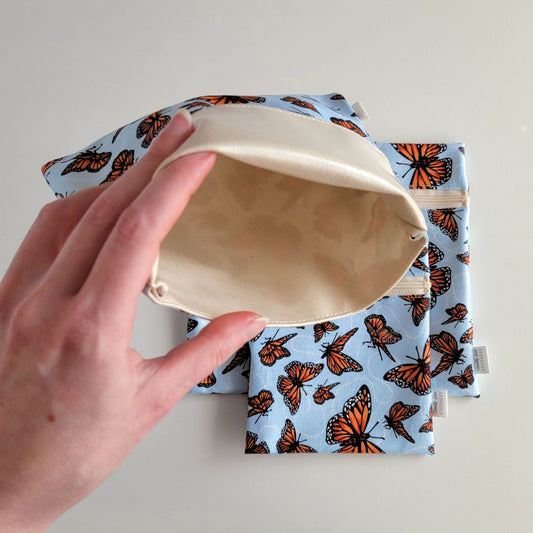 Hand holding a Monarch Blue Foldover Reusable Snack Bag open to show the lining inside, which is beige and is slightly shiny because it is water-resistant.