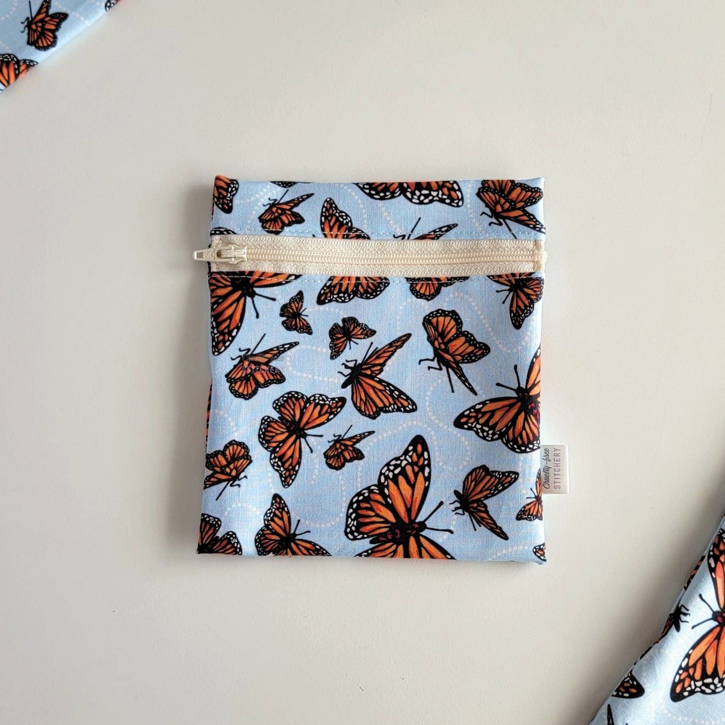 The Monarch Blue Small Zip Reusable Snack Bag, shown closed with two other bags barely visible on the edges of the photo. 