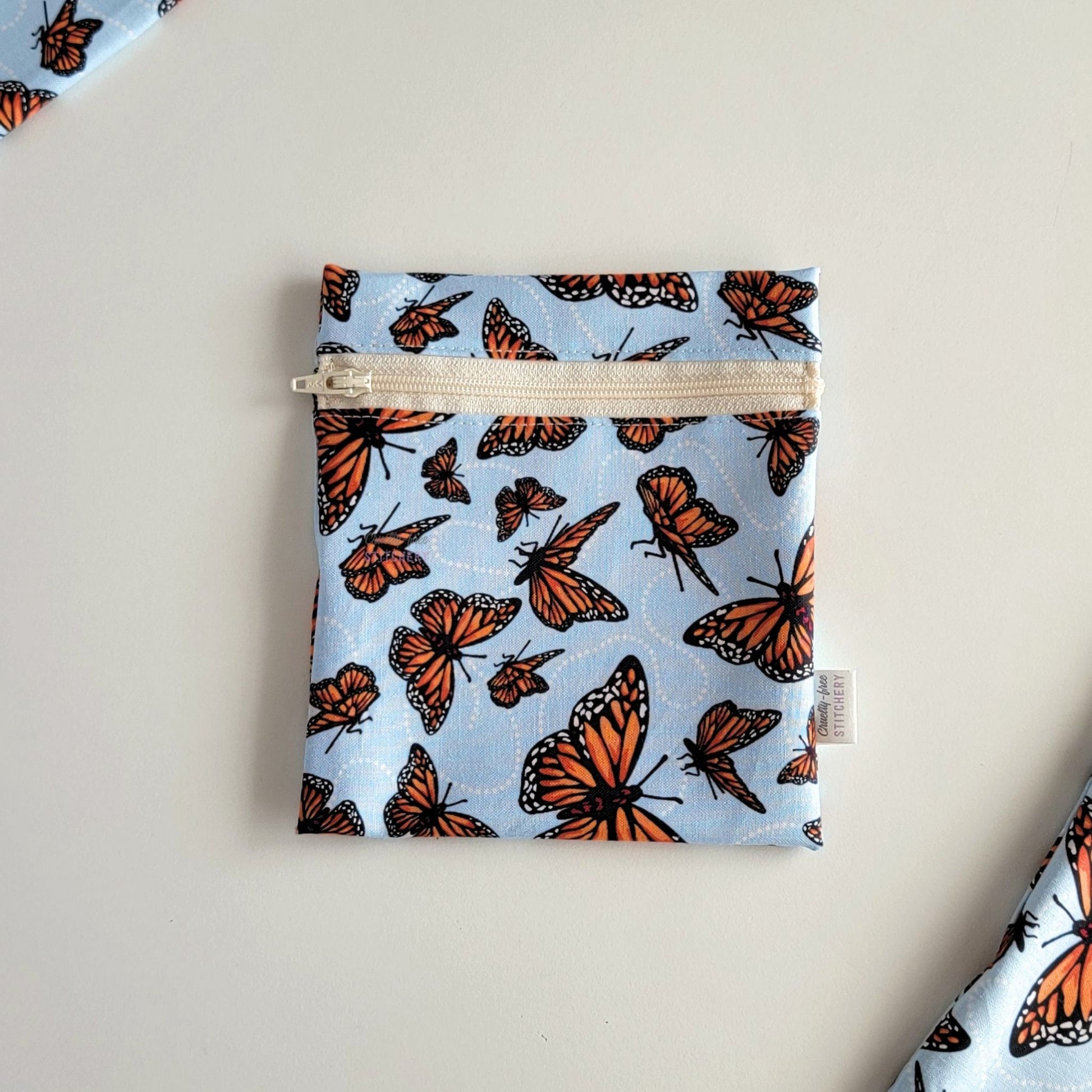 The Monarch Blue Small Zip Reusable Snack Bag, shown closed with two other bags barely visible on the edges of the photo. 