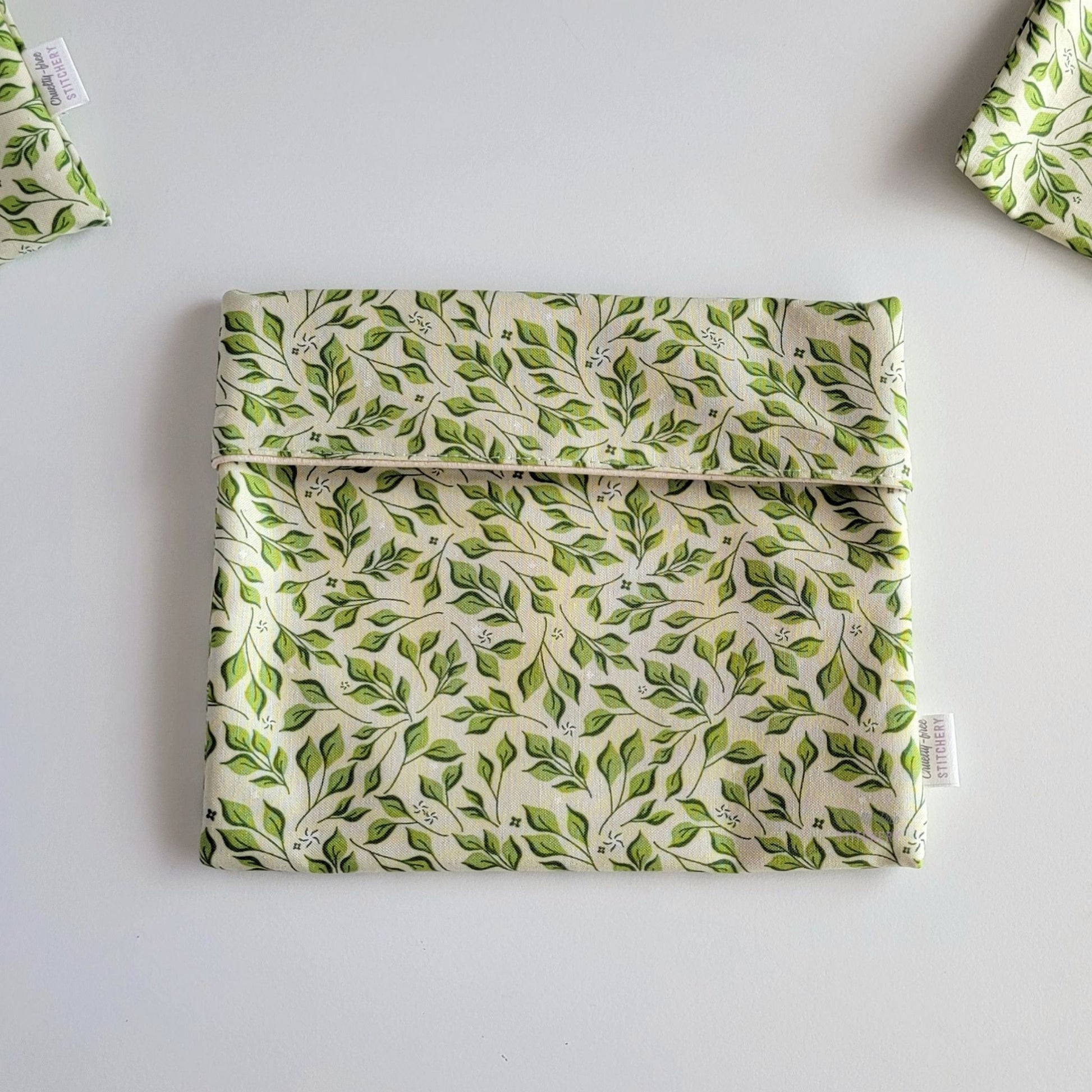 The Olive Leaves Foldover Reusable Snack Bag, shown closed with two other bags barely visible on the edges of the photo. 
