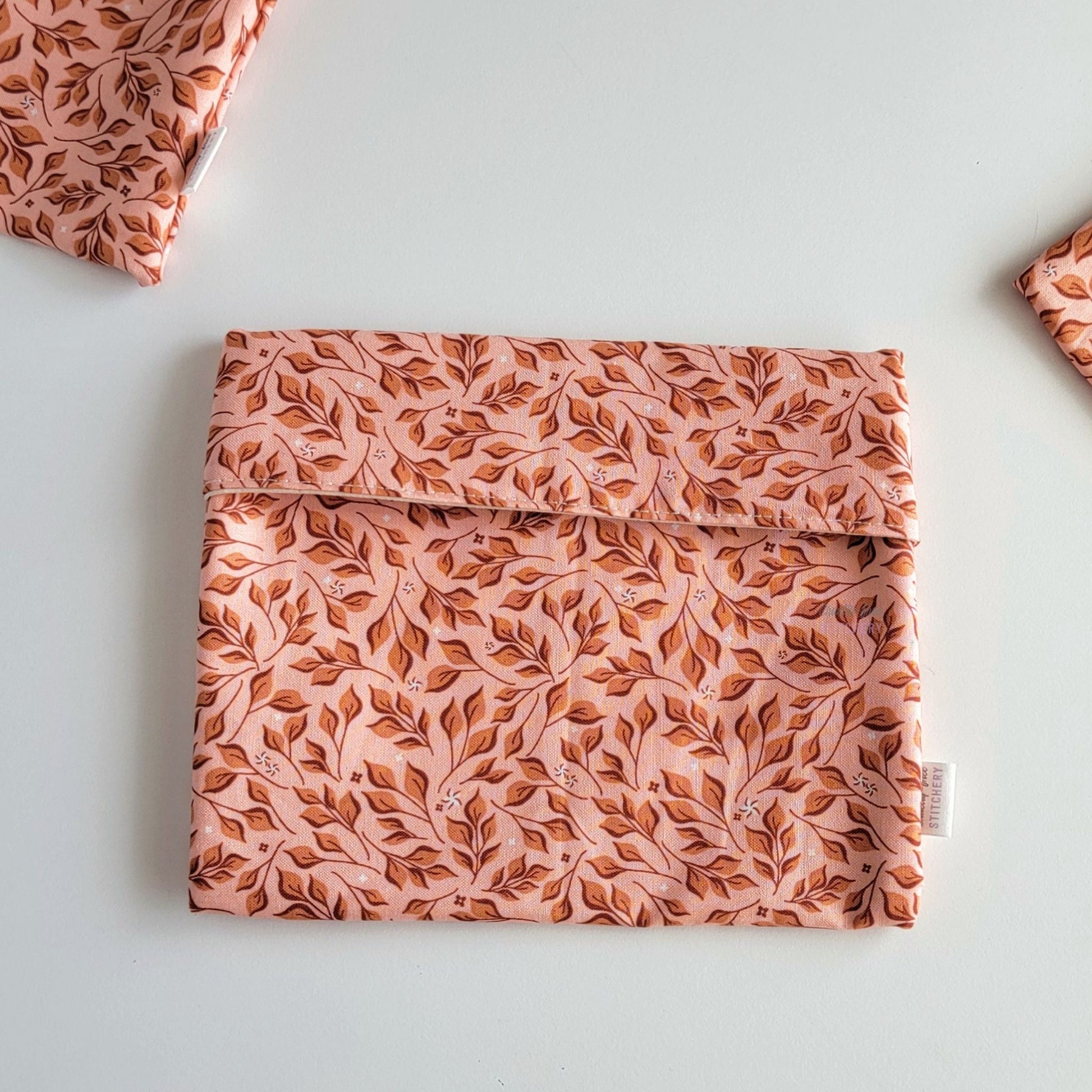 The Pink Leaves Foldover Reusable Snack Bag, shown closed with two other bags barely visible on the edges of the photo. 