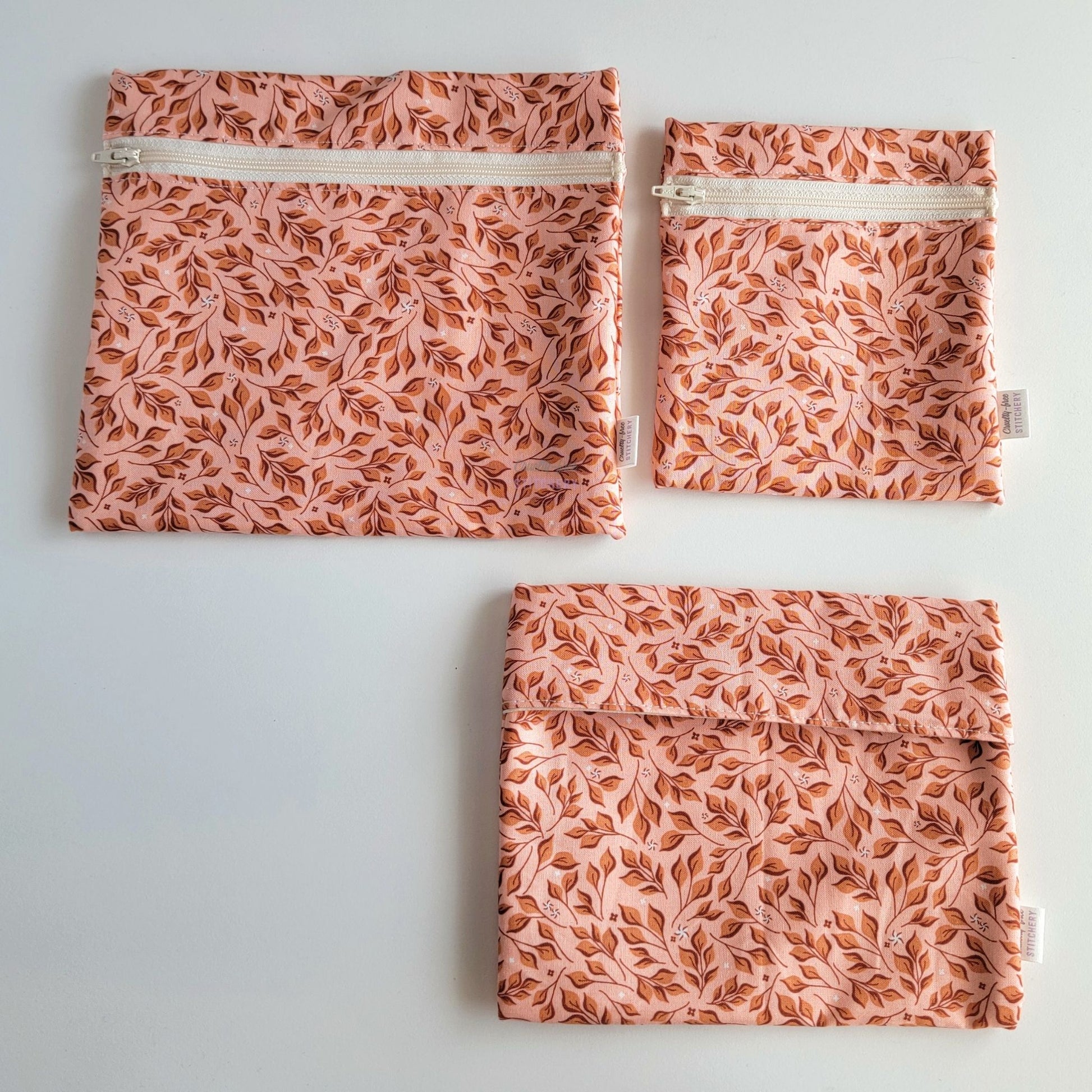 Three Pink Leaves Reusable Snack Bags arranged separately to show the difference between sizes. Large Zip is not quite double the size of the Small Zip, and the Foldover is slightly smaller than the Large Zip.