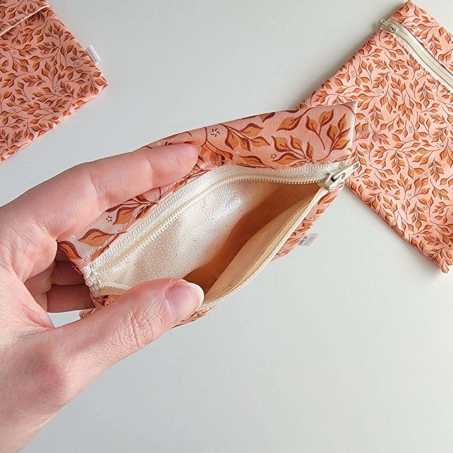 Hand holding a Pink Leaves Small Zip Reusable Snack Bag open to show the lining inside, which is beige and is slightly shiny because it is water-resistant.