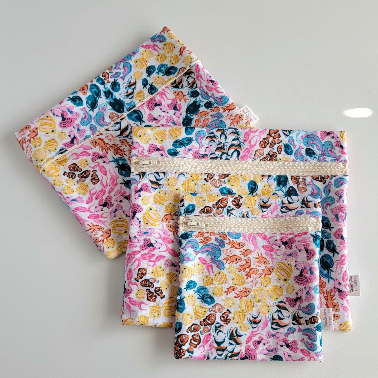 Set of three reusable snack bags with a colorful fish print, shown with the foldover style bag closed and behind the zipper styles. 