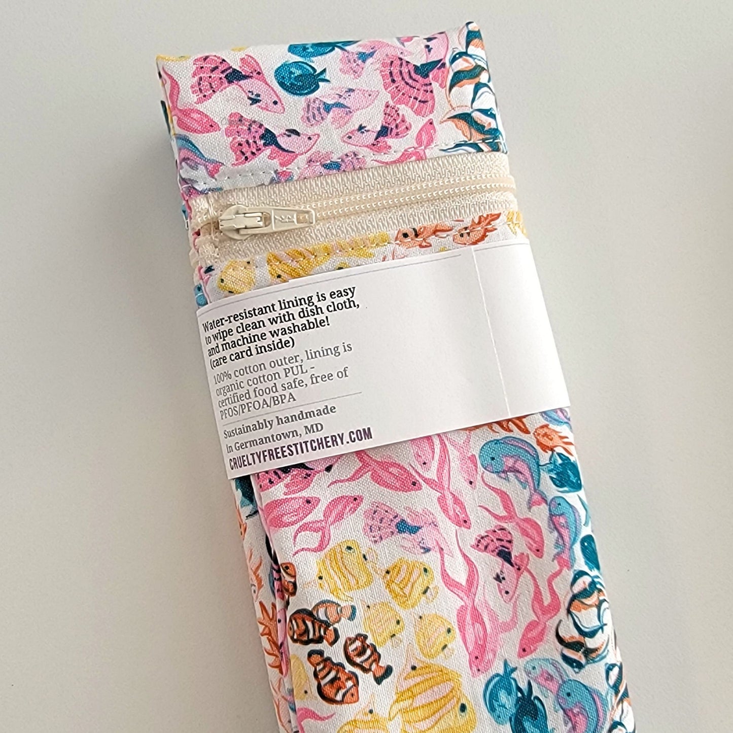 The back of the Snack Bag packaging. It says "Water resistant lining is easy to wipe clean with dish cloth, and machine washable. Care card inside. 100% cotton outer, lining is organic cotton PUL, cerfitied food-safe, free of PFOS, PFOA, BPA. Sustainable handmade in Germantown, MD" and our website url.