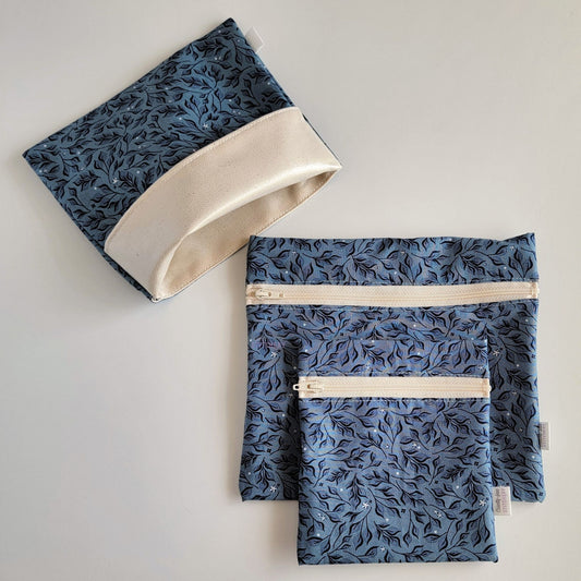 Set of three reusable snack bags with a Dark Blue leaves print. Two have zippers, one large and one small, and one is a fold-over style. The fold-over one is unfolded to show the beige lining that matches the zippers.