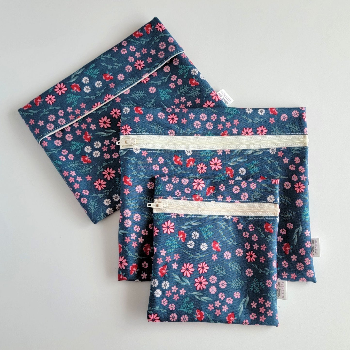 Set of three reusable snack bags with a teal with pink flowers print, shown with the foldover style bag closed and behind the zipper styles. 