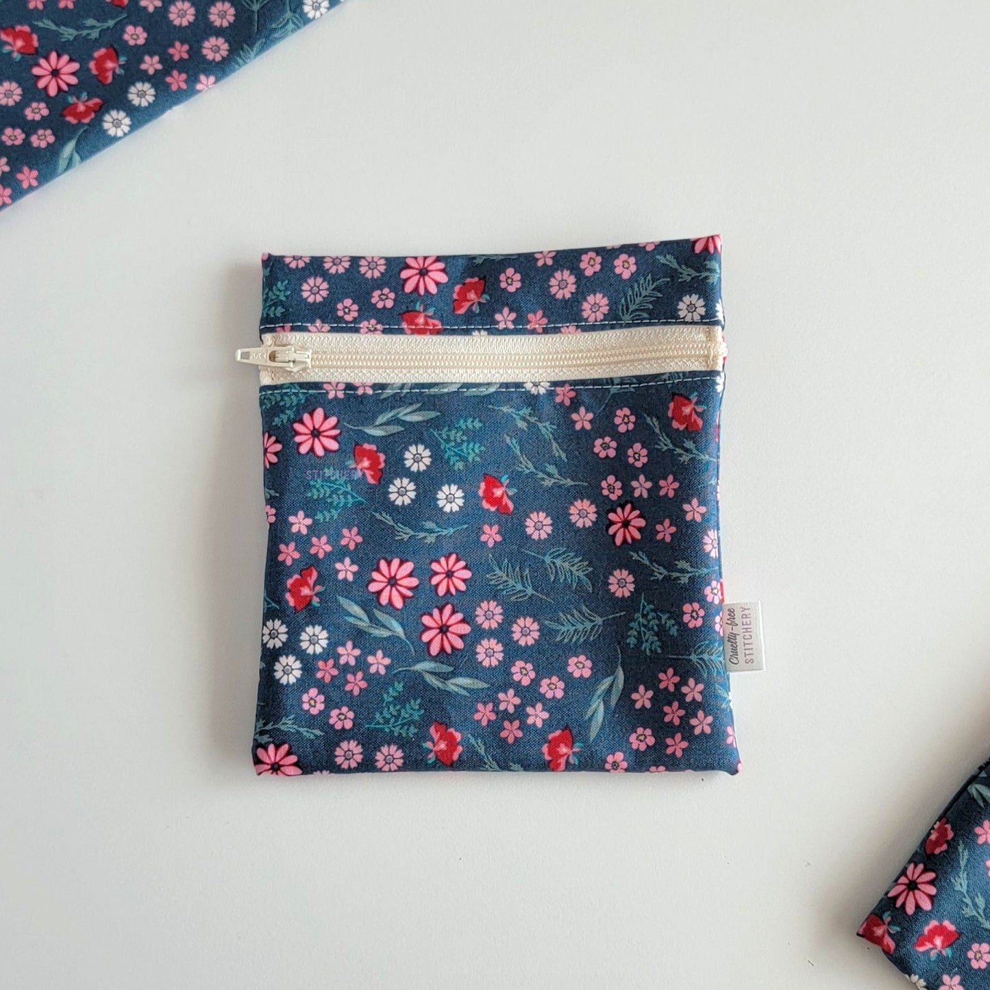 The Teal Pink Floral Small Zip Reusable Snack Bag, shown closed with two other bags barely visible on the edges of the photo. 
