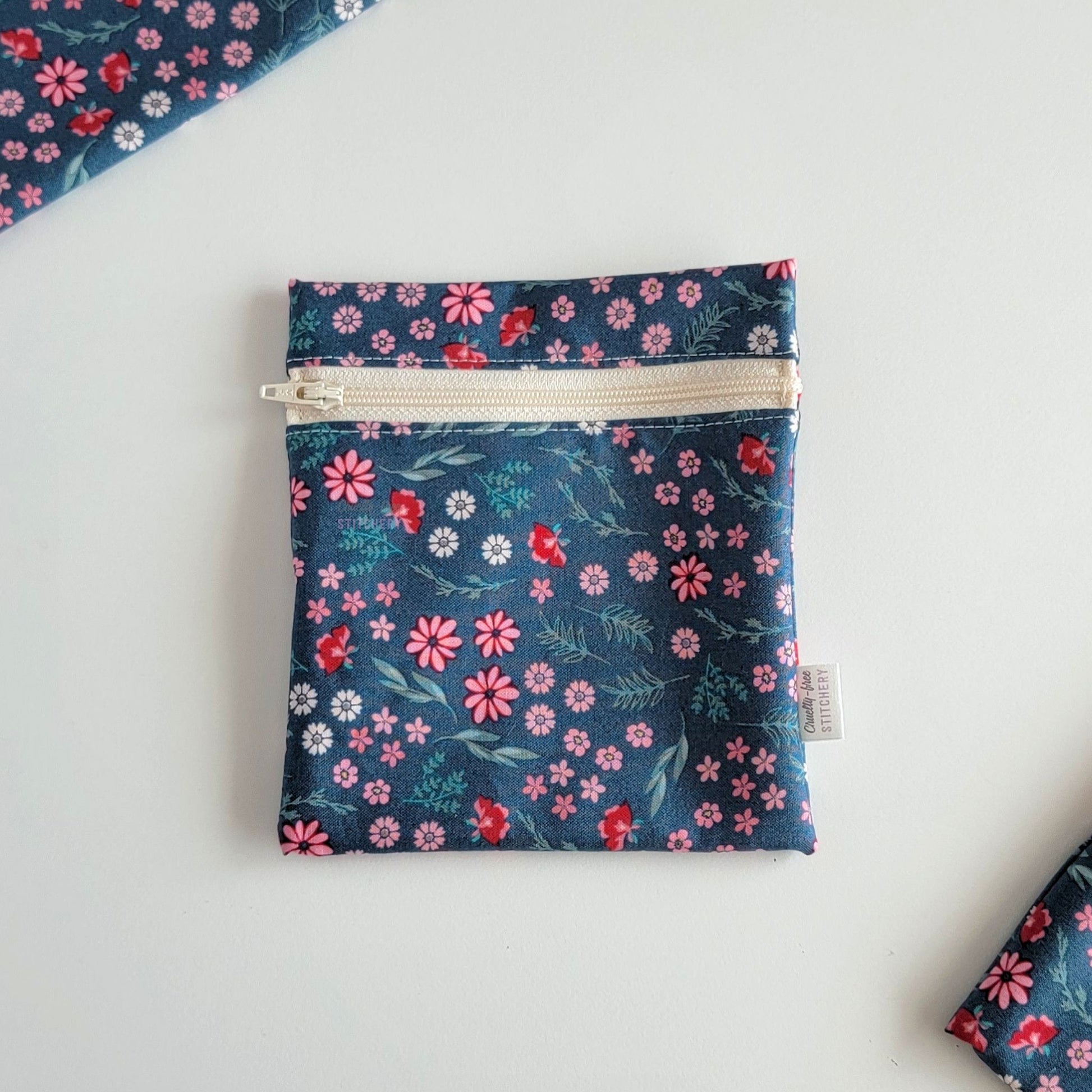 The Teal Pink Floral Small Zip Reusable Snack Bag, shown closed with two other bags barely visible on the edges of the photo. 
