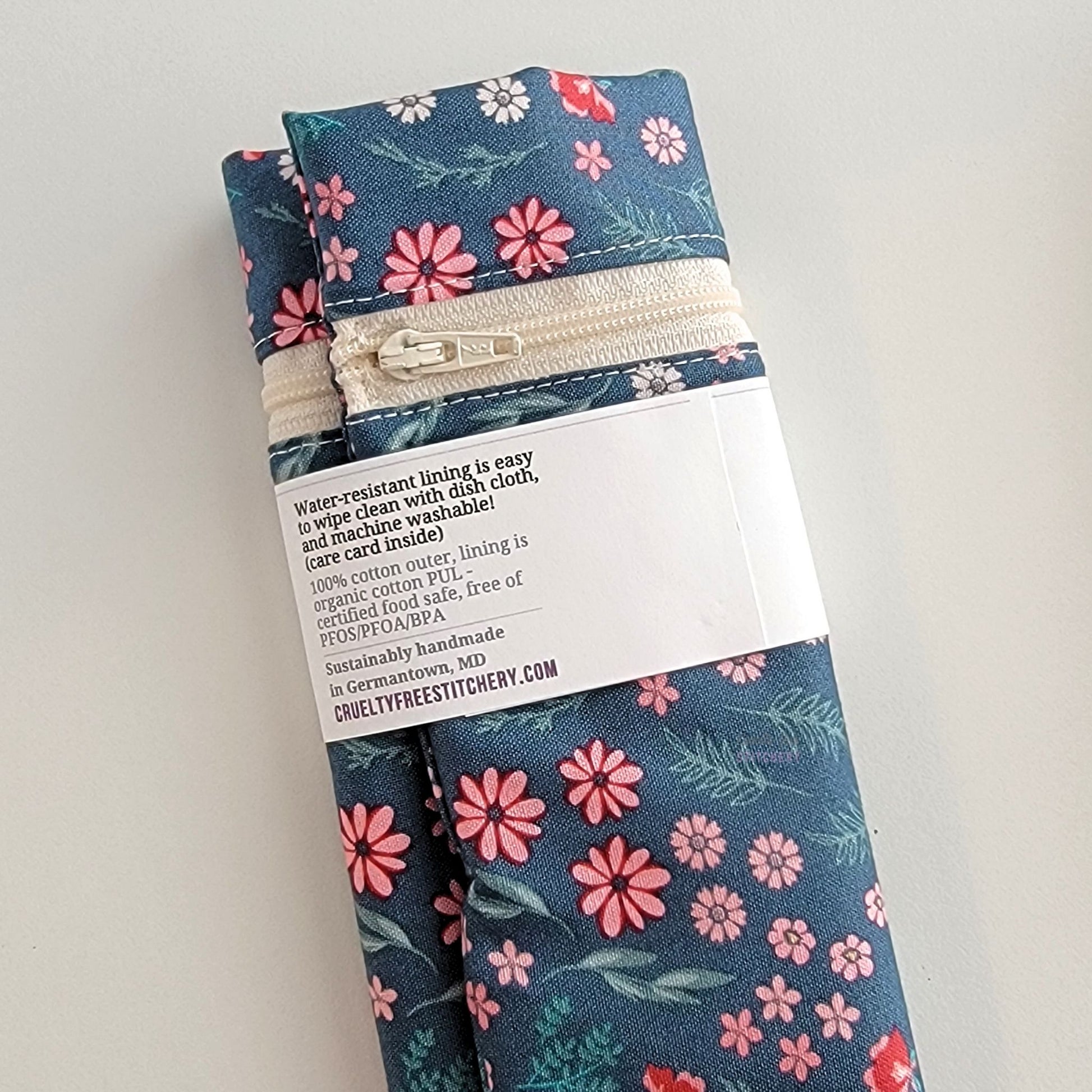 The back of the Snack Bag packaging. It says "Water resistant lining is easy to wipe clean with dish cloth, and machine washable. Care card inside. 100% cotton outer, lining is organic cotton PUL, cerfitied food-safe, free of PFOS, PFOA, BPA. Sustainable handmade in Germantown, MD" and our website url.