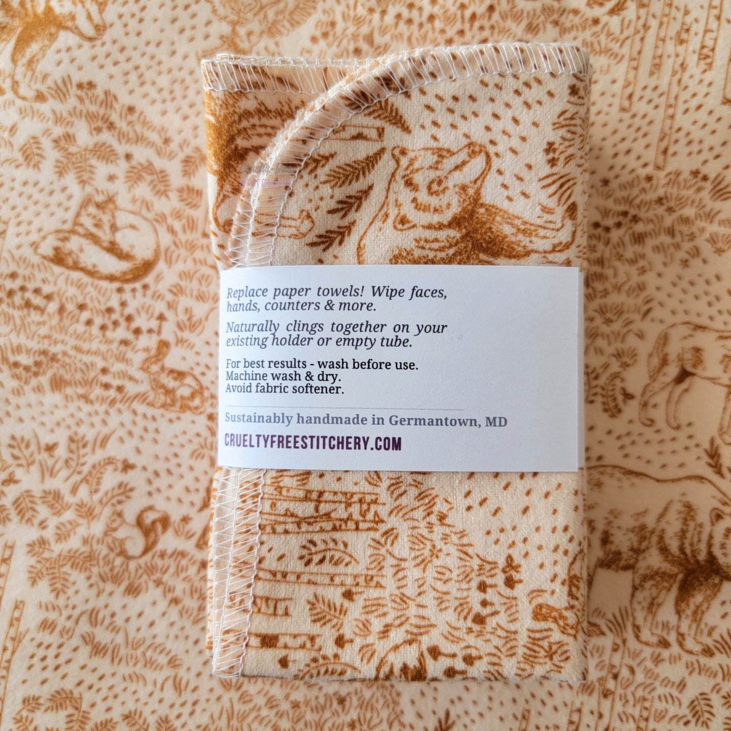 The back of a packaged bundle of the Acorn Woodland NonPaper Towels. The tag reads "Replace paper towels! Wipe faces, hands, counters, and more. Naturally clings together on your existing holder or empty tube. For best results - wash before use. Machine wash and dry. Avoid fabric softener. Sustainable handmade in Germantown, Maryland. CrueltyFreeStitchery dot com."