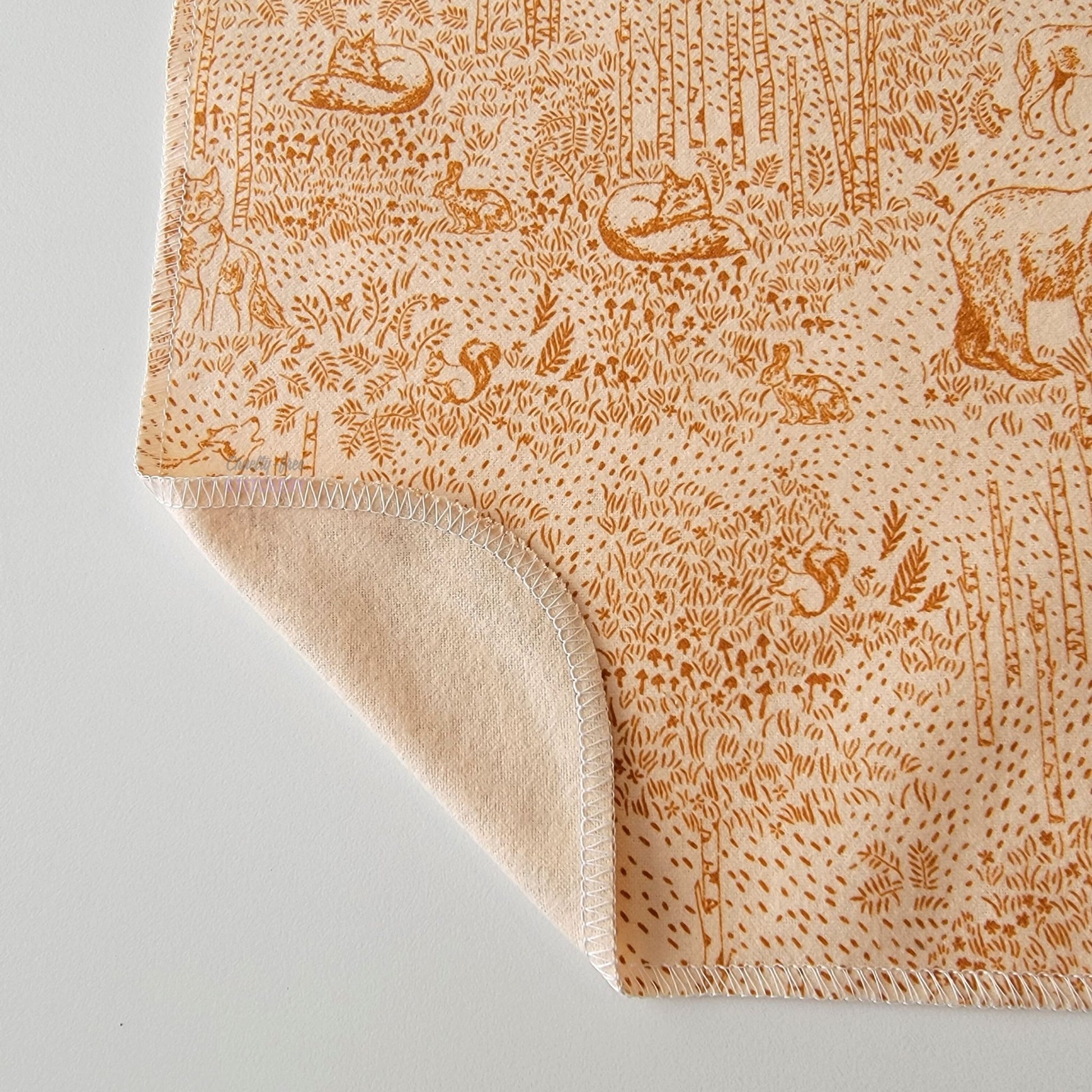 The Acorn Woodland NonPaper Towel, shown close-up with the bottom corner folded back to show they are unprinted on the back side, and are one layer.