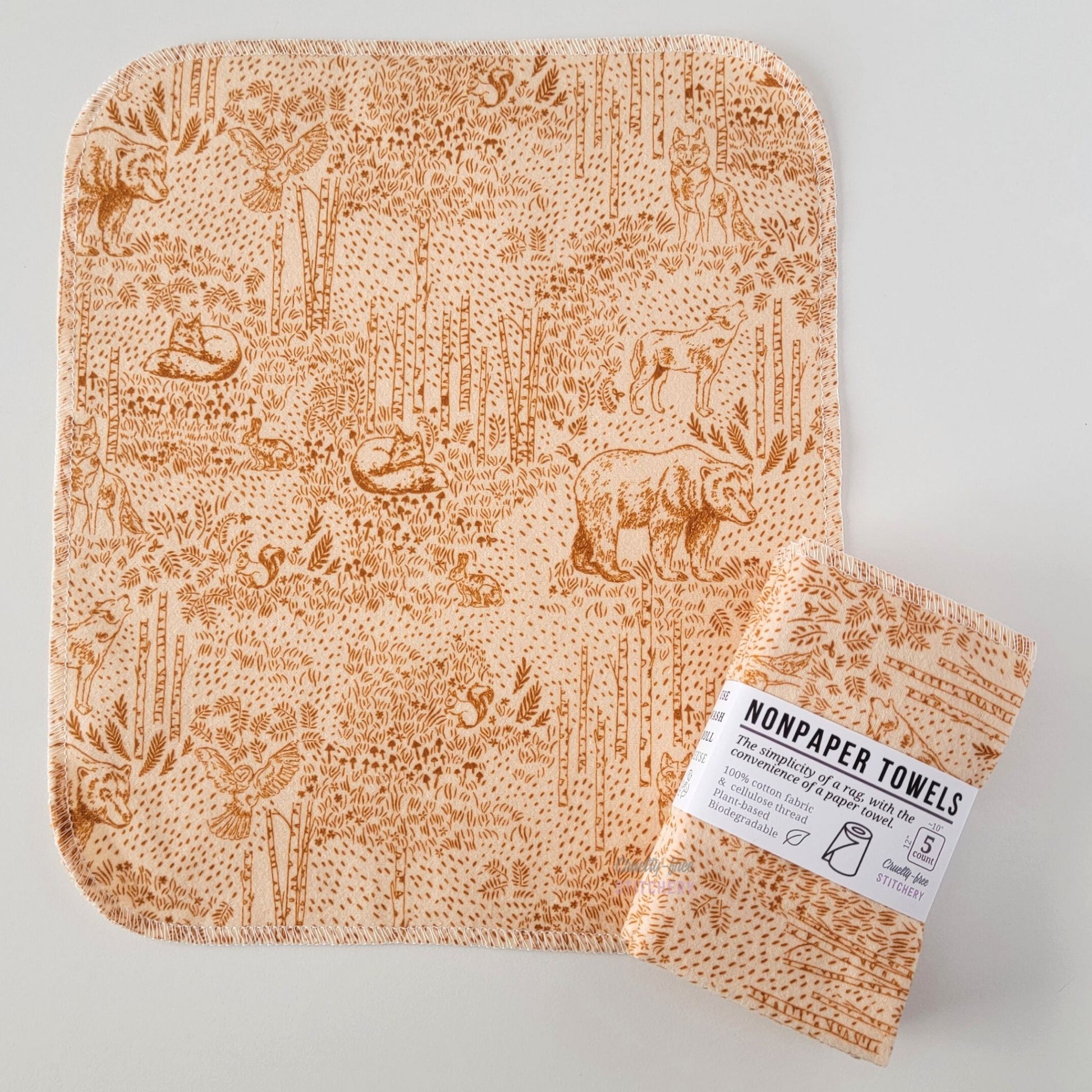 An unfolded Acorn Woodland NonPaper Towel, next to a bundled 5-pack. The towel is a rectangle with rounded corners, stitched around the edges with white thread. The bundled pack is folded up with a paper wrapper that says "NonPaper Towels, the simplicity of a rag with the convenience of a paper towel"