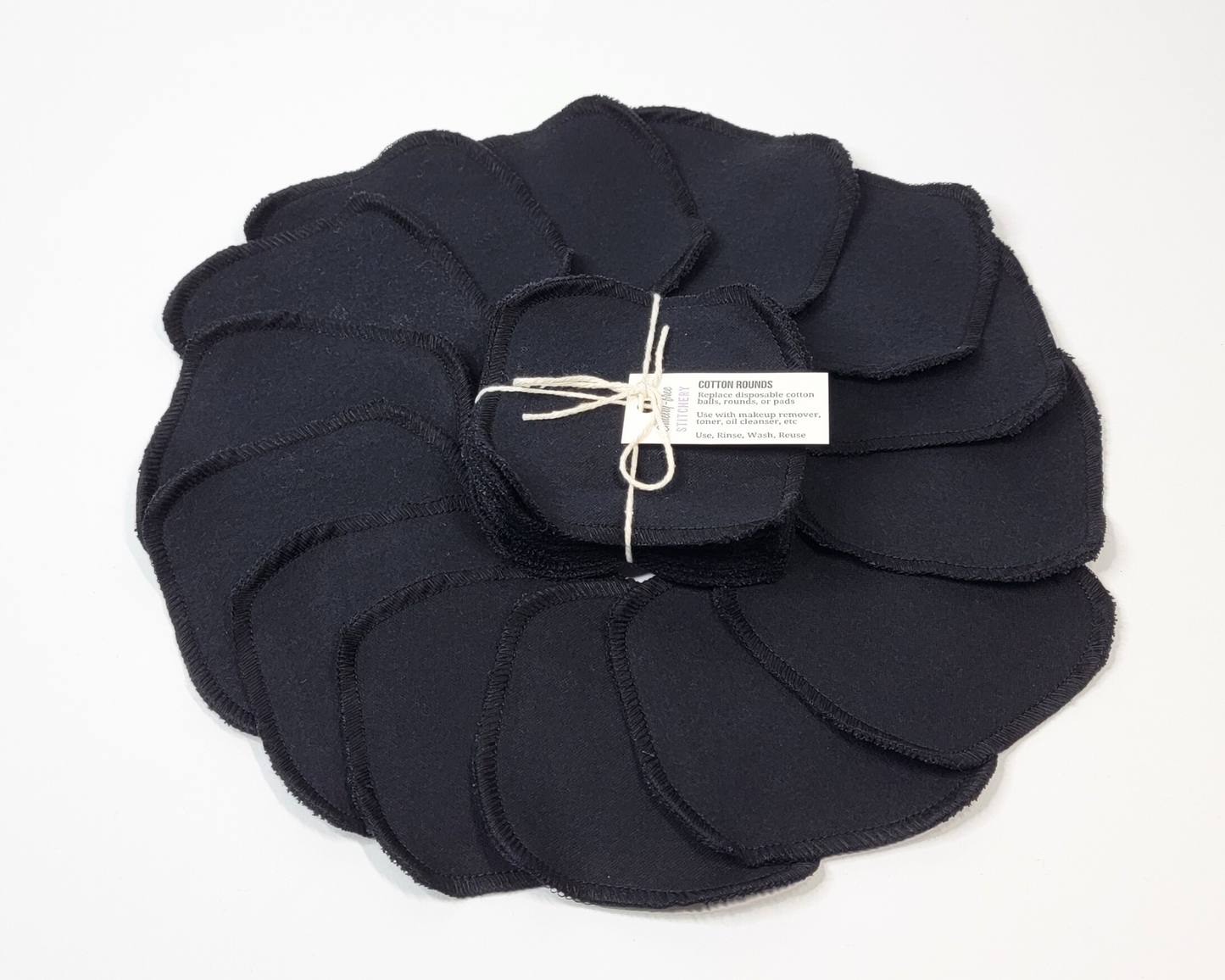 Black reusable cotton rounds arranged in a circle, with a bundled pack in the center. They are solid black with black stitching on the edges.