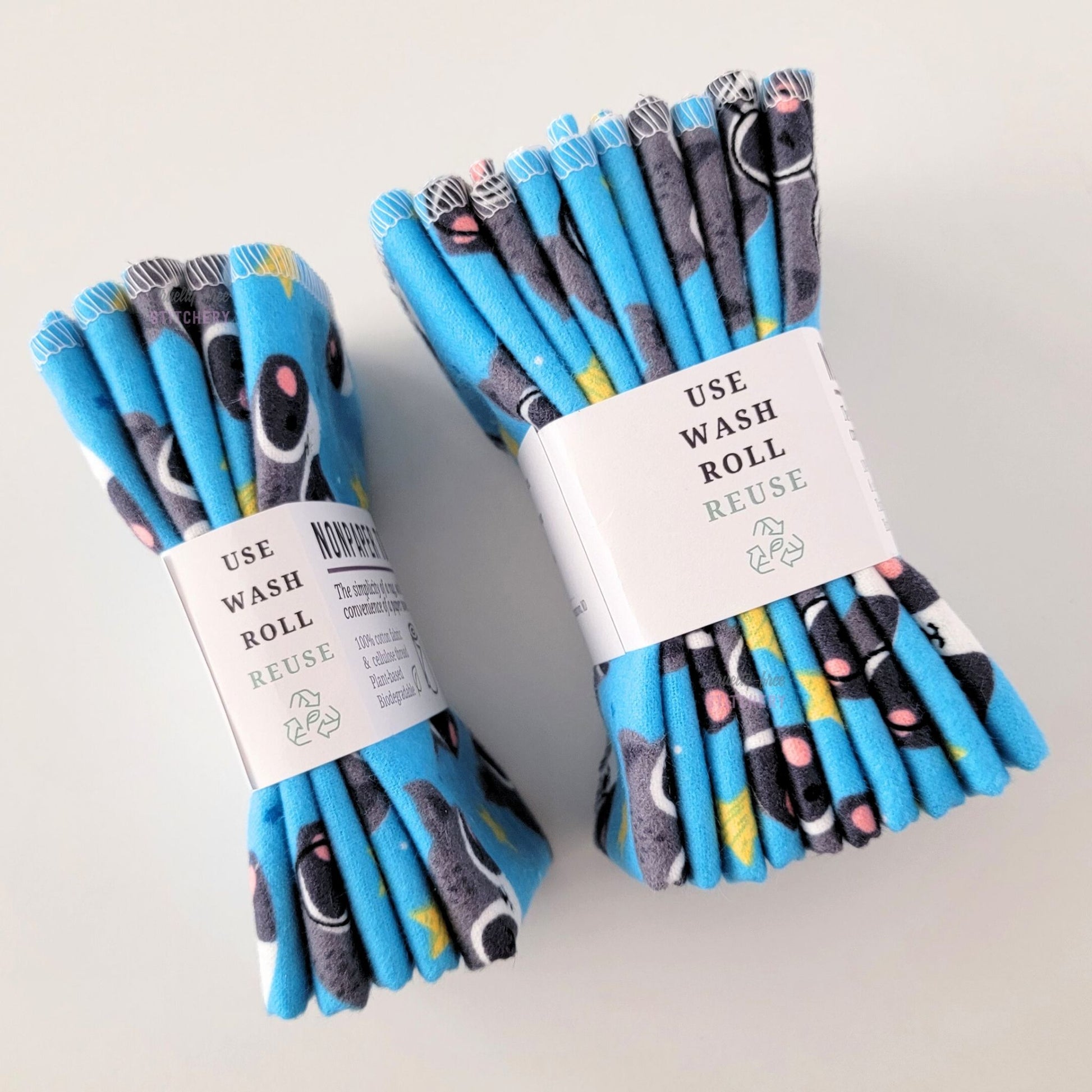 Two packages of the Blue Raccoons NonPaper Towels, shown on their side so display the 5-pack and 10-packs. The side of the paper tag says "use, wash, roll, reuse" and has the recycling logo with a leaf in the center, to symbolize they are biodegradable.