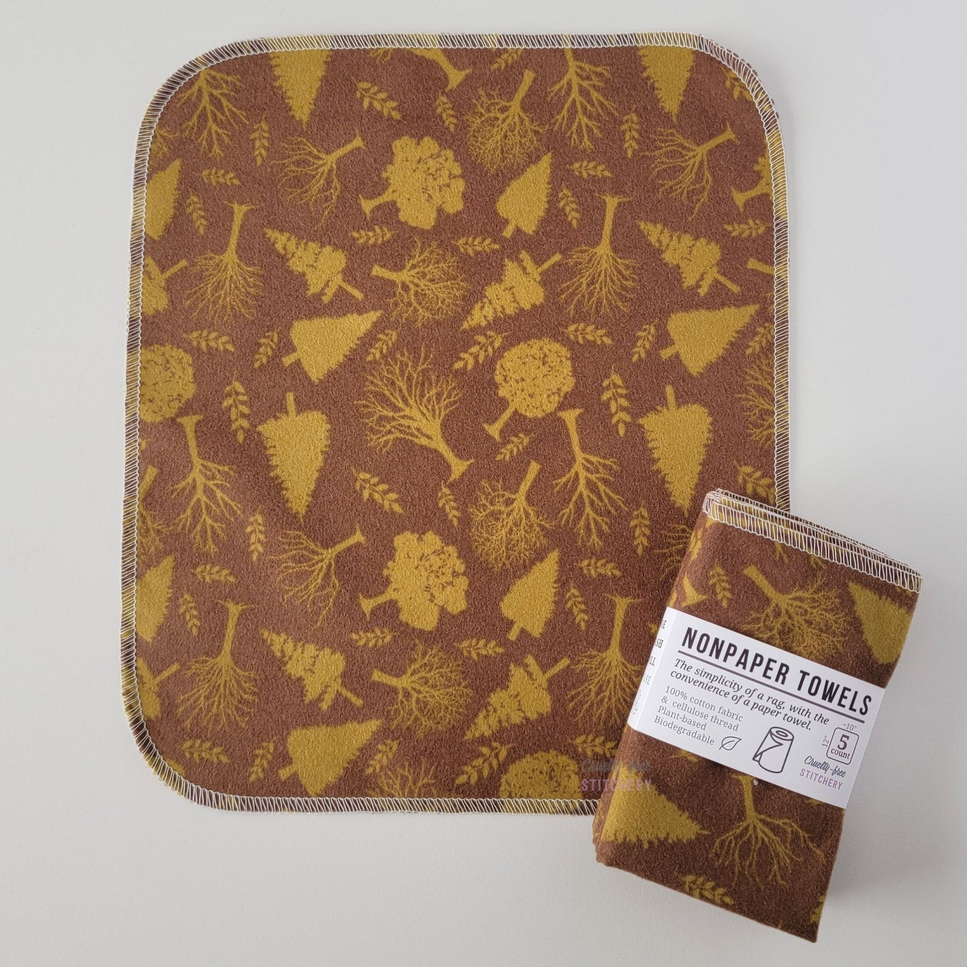 An unfolded Brown Trees NonPaper Towel, next to a bundled 5-pack. The towel is a rectangle with rounded corners, stitched around the edges with white thread. The bundled pack is folded up with a paper wrapper that says "NonPaper Towels, the simplicity of a rag with the convenience of a paper towel"
