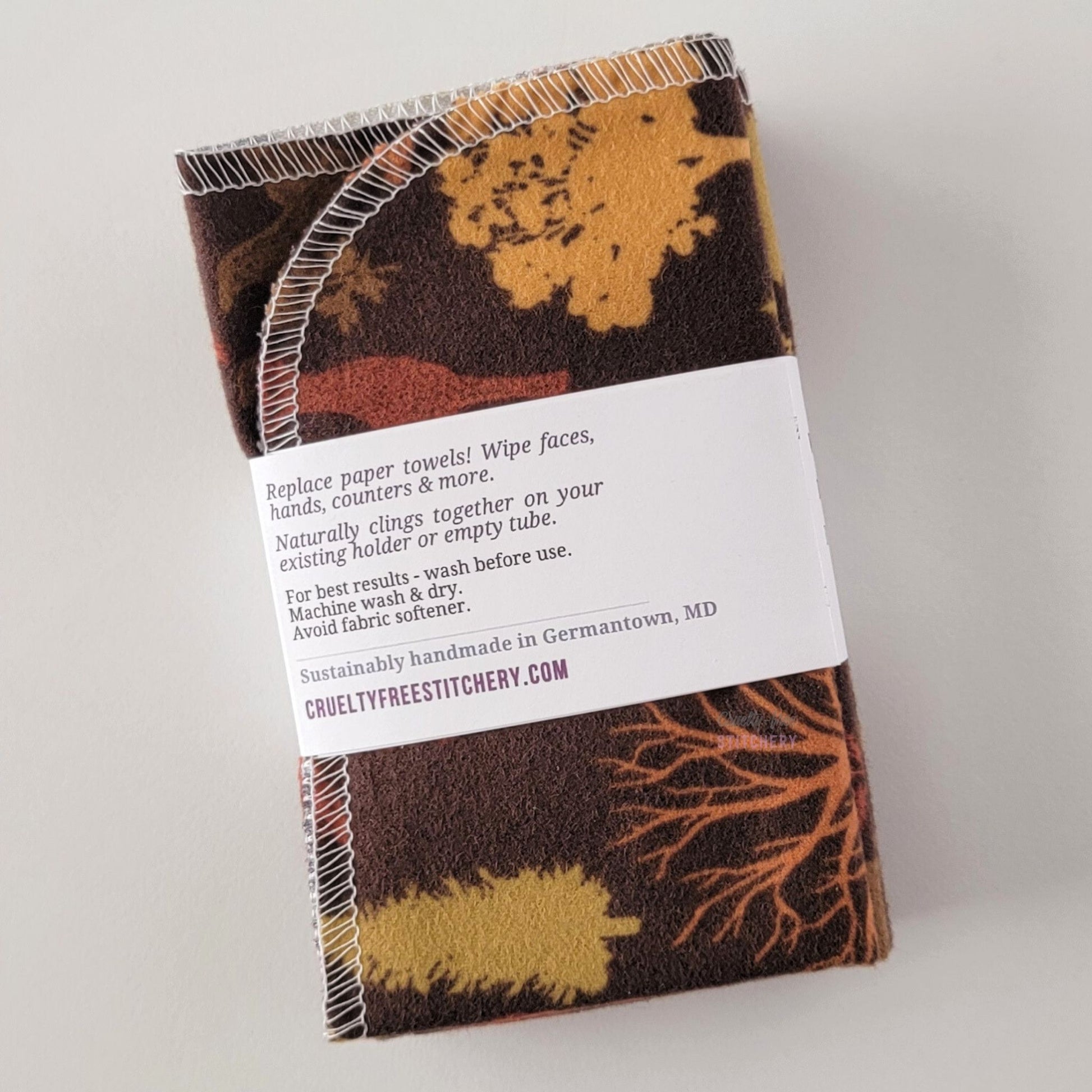 The back of a packaged bundle of the Brown Woodland NonPaper Towels. The tag reads "Replace paper towels! Wipe faces, hands, counters, and more. Naturally clings together on your existing holder or empty tube. For best results - wash before use. Machine wash and dry. Avoid fabric softener. Sustainable handmade in Germantown, Maryland. CrueltyFreeStitchery dot com."