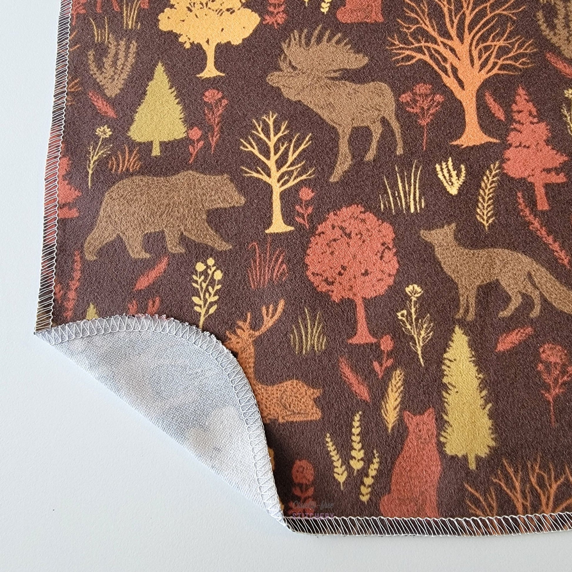 The Brown Woodland NonPaper Towel, shown close-up with the bottom corner folded back to show they are unprinted on the back side, and are one layer.