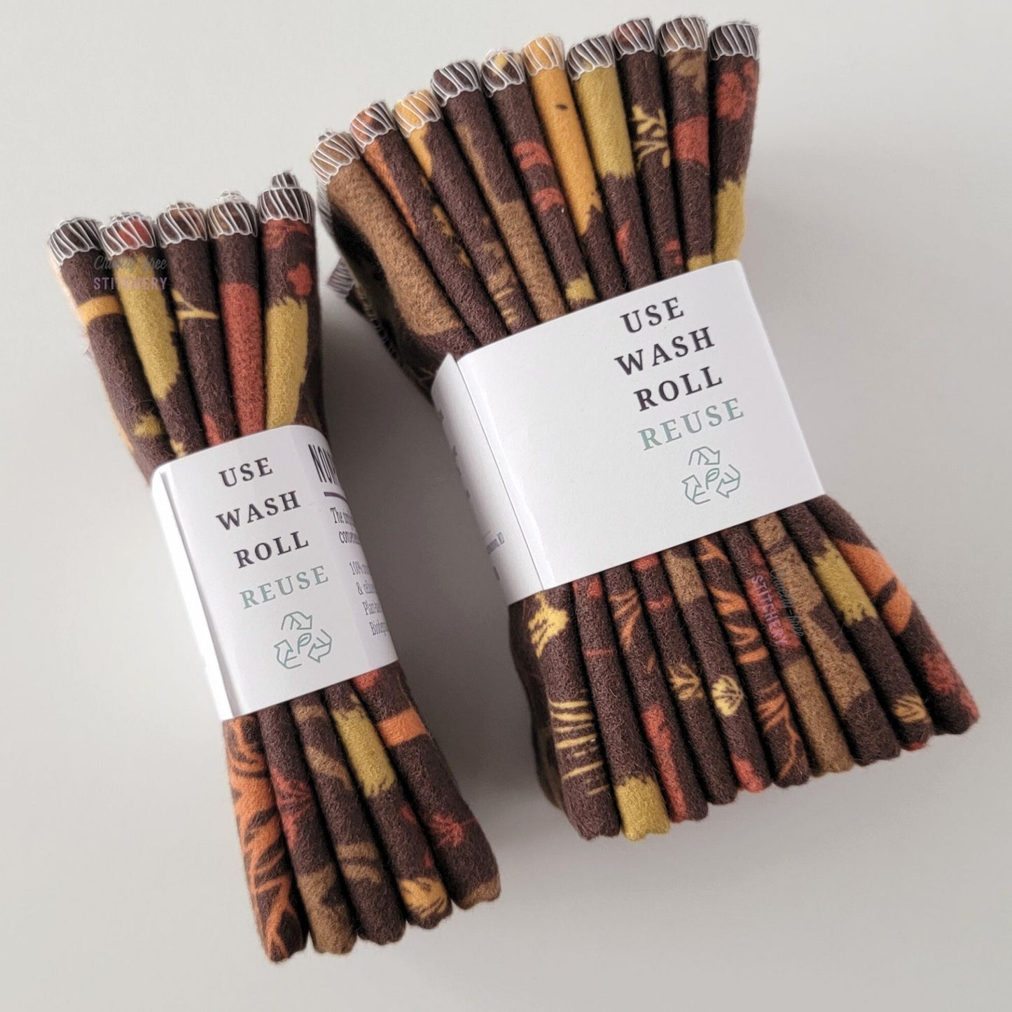 Two packages of the Brown Woodland NonPaper Towels, shown on their side so display the 5-pack and 10-packs. The side of the paper tag says "use, wash, roll, reuse" and has the recycling logo with a leaf in the center, to symbolize they are biodegradable.
