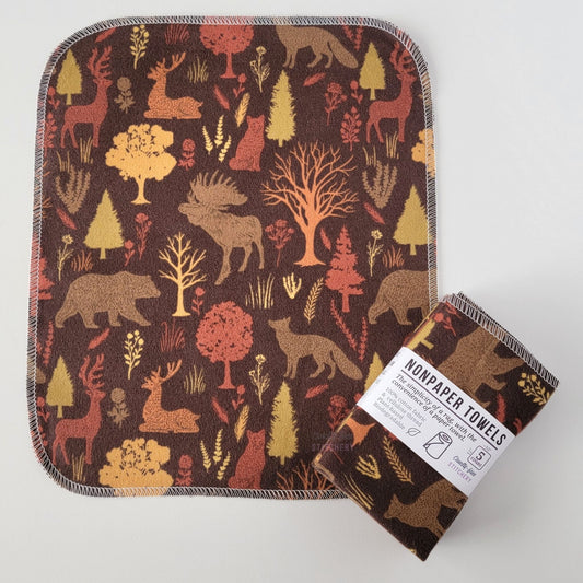 An unfolded Brown Woodland NonPaper Towel, next to a bundled 5-pack. The towel is a rectangle with rounded corners, stitched around the edges with white thread. The bundled pack is folded up with a paper wrapper that says "NonPaper Towels, the simplicity of a rag with the convenience of a paper towel"
