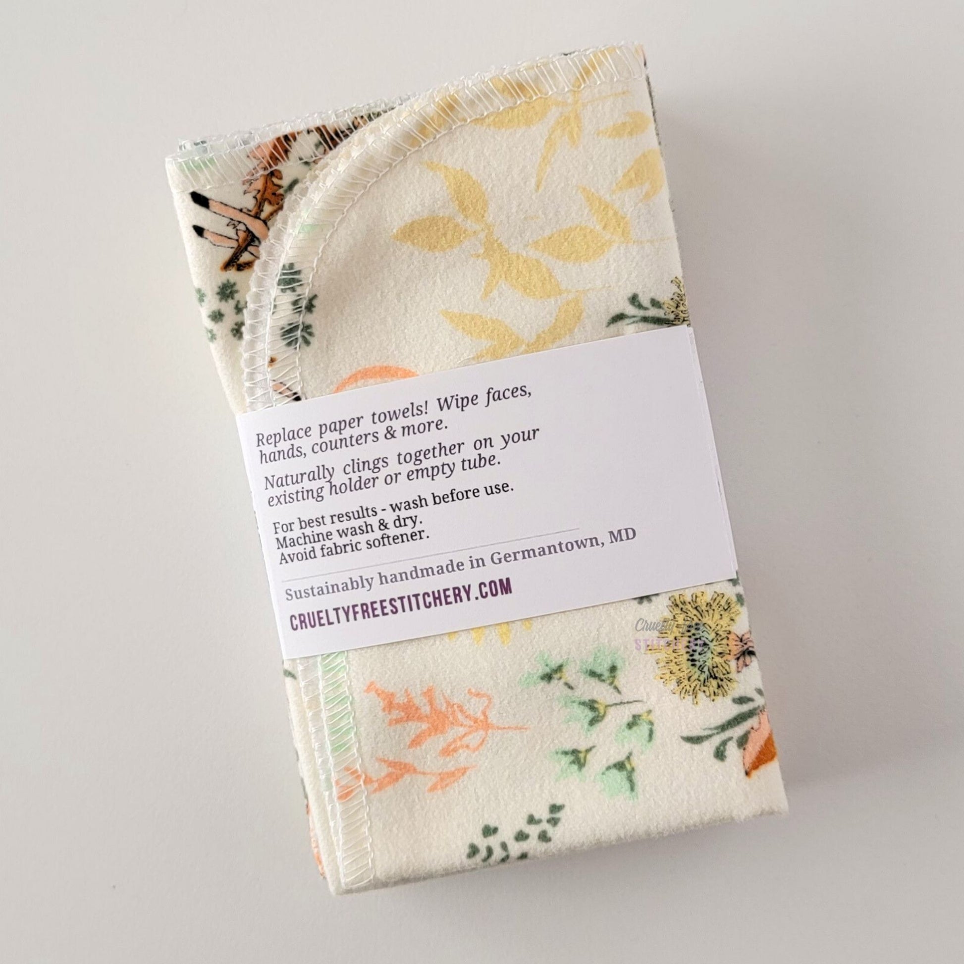 The back of a packaged bundle of the Dandelion Doe NonPaper Towels. The tag reads "Replace paper towels! Wipe faces, hands, counters, and more. Naturally clings together on your existing holder or empty tube. For best results - wash before use. Machine wash and dry. Avoid fabric softener. Sustainable handmade in Germantown, Maryland. CrueltyFreeStitchery dot com."