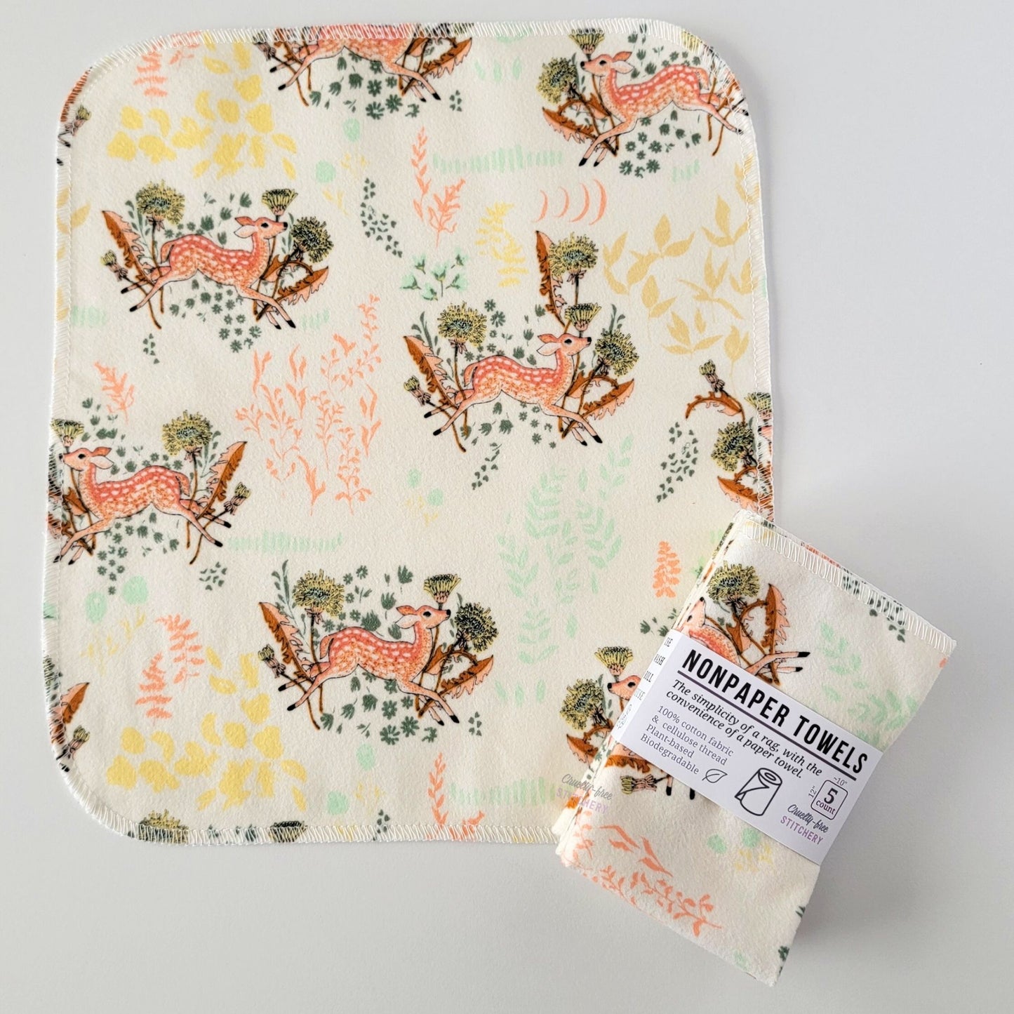 An unfolded Dandelion Doe NonPaper Towel, next to a bundled 5-pack. The towel is a rectangle with rounded corners, stitched around the edges with white thread. The bundled pack is folded up with a paper wrapper that says "NonPaper Towels, the simplicity of a rag with the convenience of a paper towel"