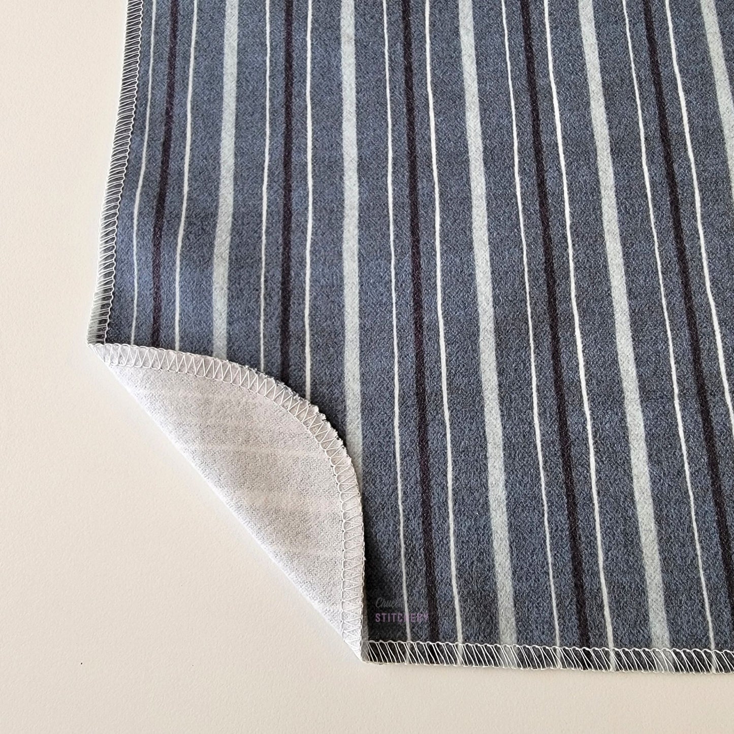 The Deep Blue Stripe NonPaper Towel, shown close-up with the bottom corner folded back to show they are unprinted on the back side, and are one layer.