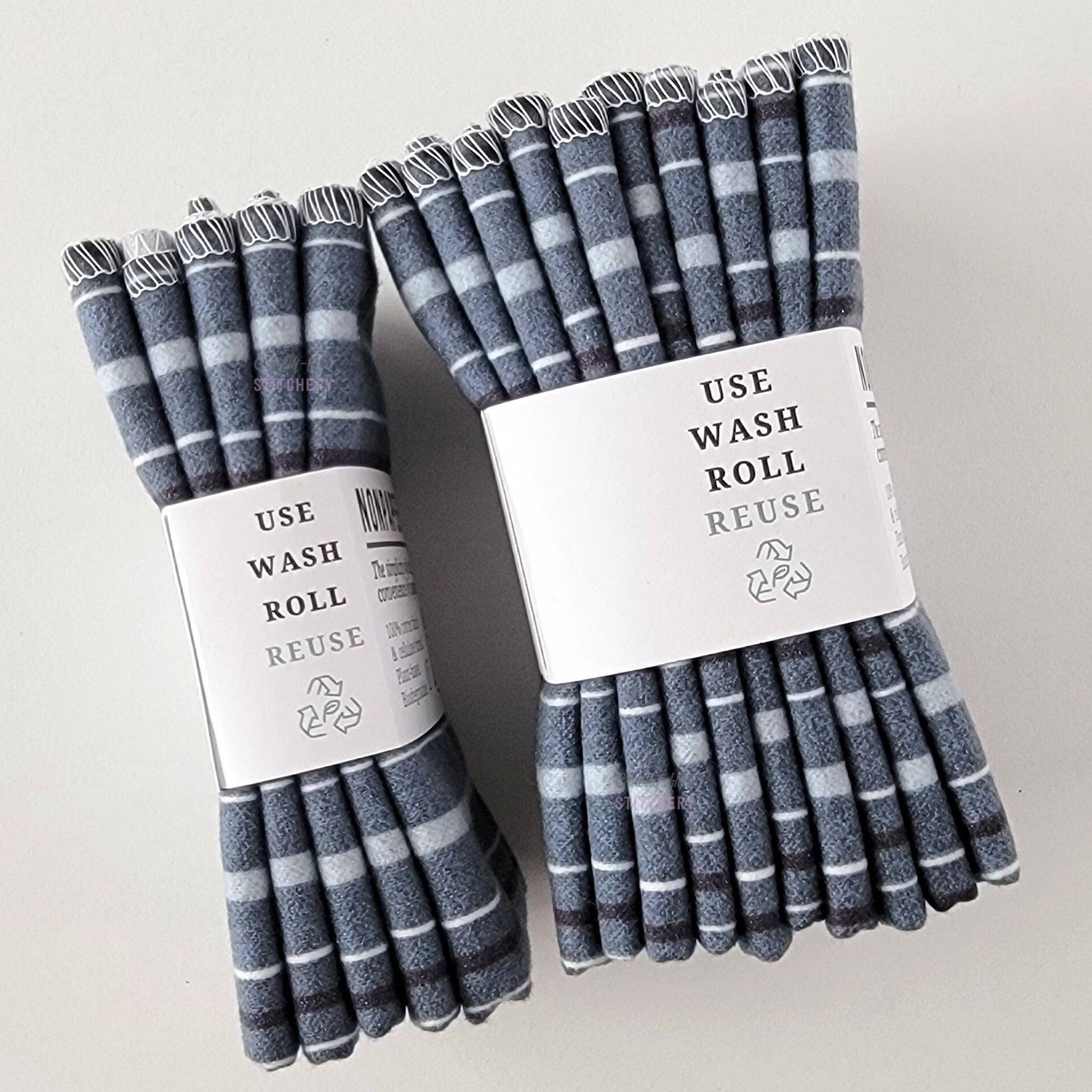 Two packages of the Deep Blue Stripe NonPaper Towels, shown on their side to display the 5-pack and 10-packs. The side of the paper tag says "use, wash, roll, reuse" and has the recycling logo with a leaf in the center, to symbolize they are biodegradable.