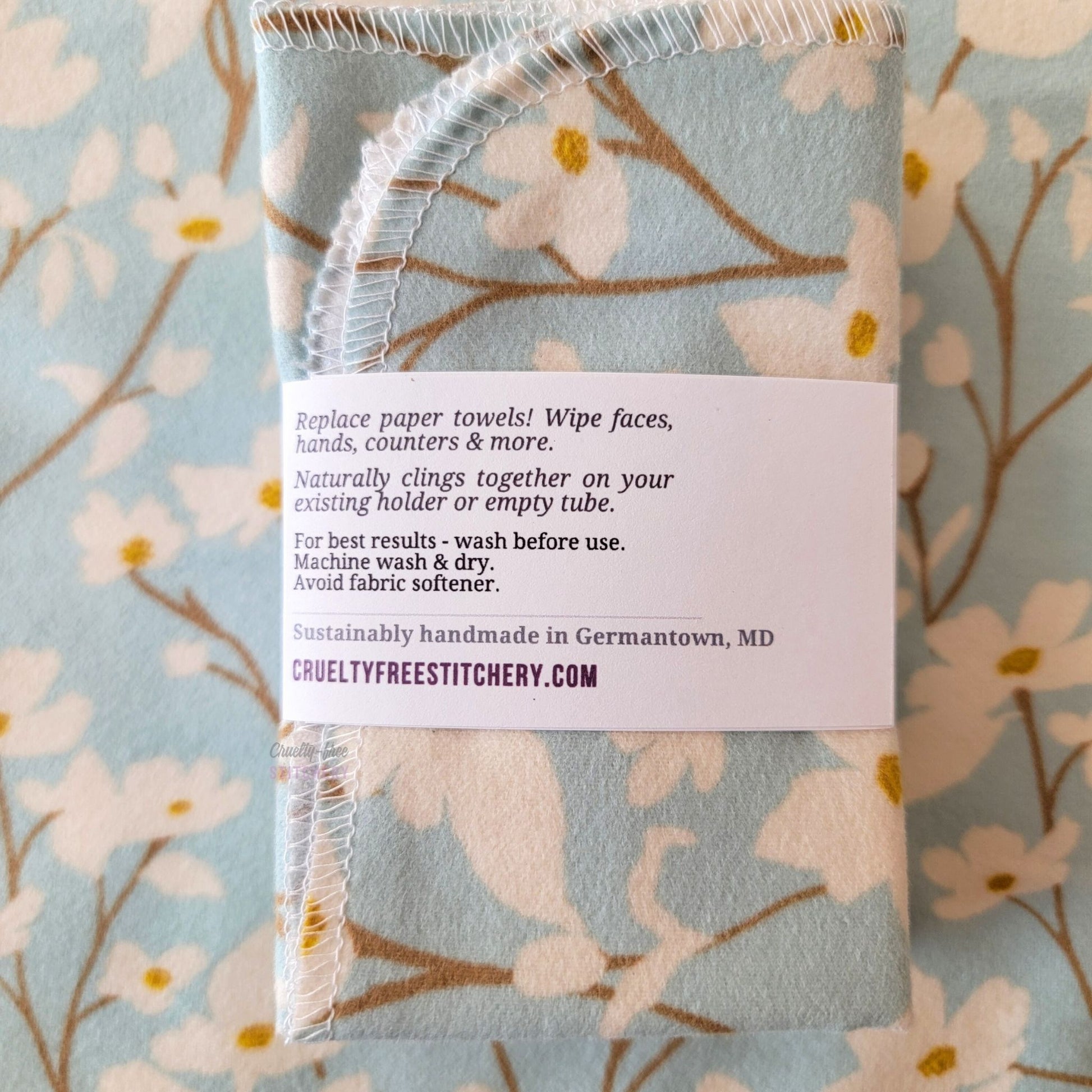 The back of a packaged bundle of the Dogwood Sky NonPaper Towels. The tag reads "Replace paper towels! Wipe faces, hands, counters, and more. Naturally clings together on your existing holder or empty tube. For best results - wash before use. Machine wash and dry. Avoid fabric softener. Sustainable handmade in Germantown, Maryland. CrueltyFreeStitchery dot com."
