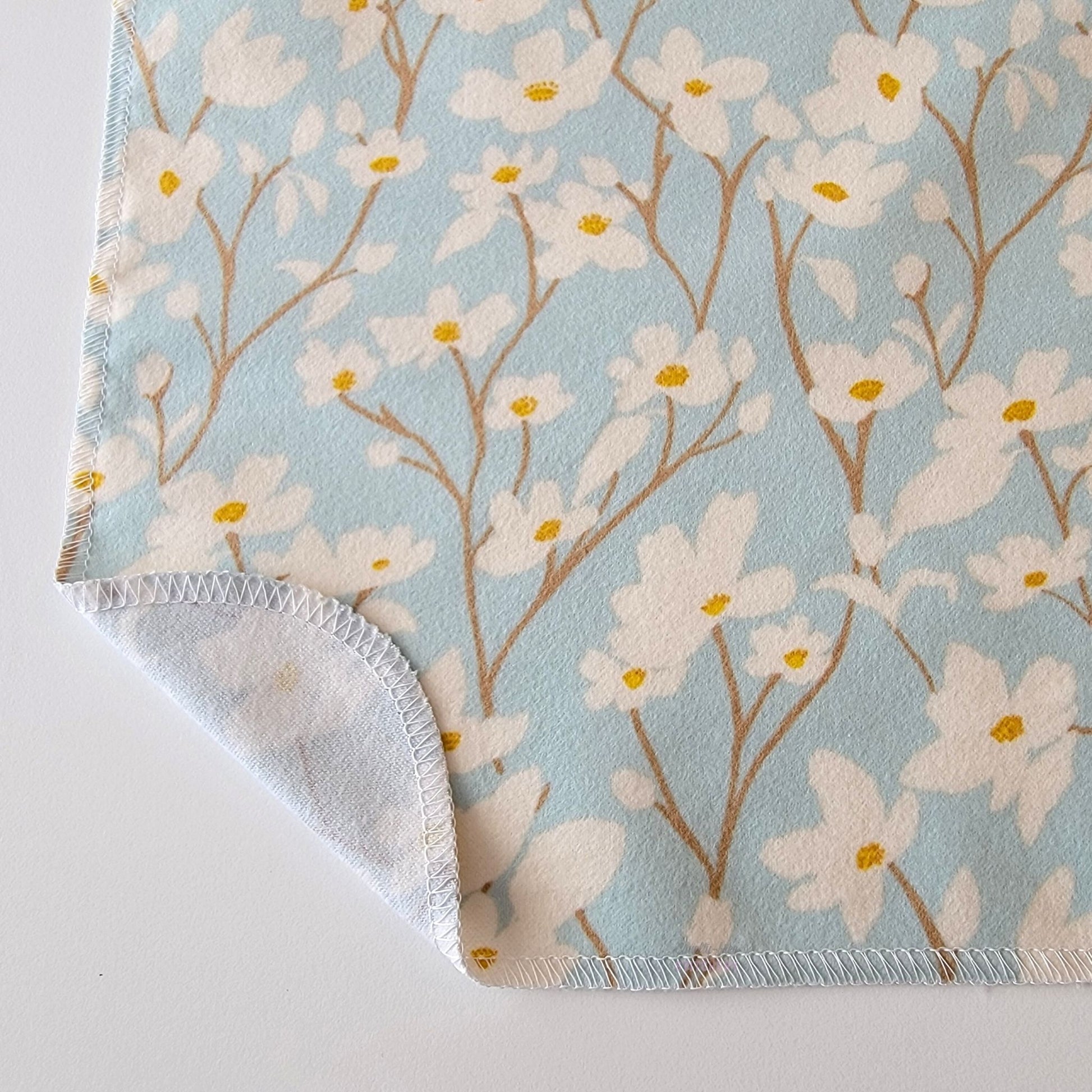 The Dogwood Sky NonPaper Towel, shown close-up with the bottom corner folded back to show they are unprinted on the back side, and are one layer.
