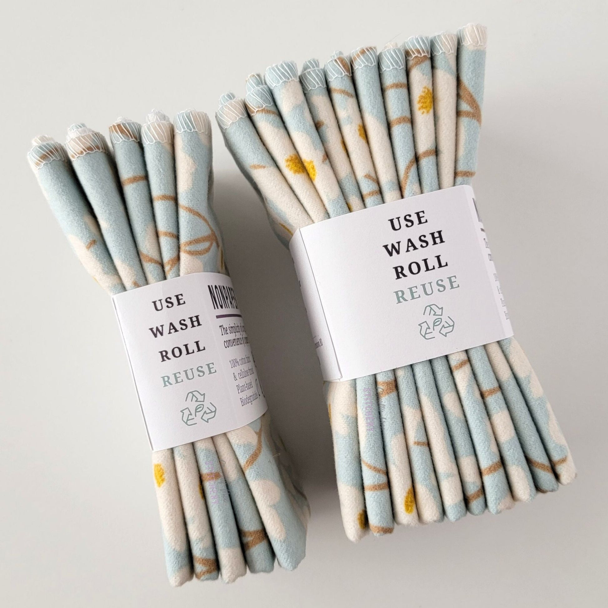 Two packages of the Dogwood Sky NonPaper Towels, shown on their side to display the 5-pack and 10-packs. The side of the paper tag says "use, wash, roll, reuse" and has the recycling logo with a leaf in the center, to symbolize they are biodegradable.