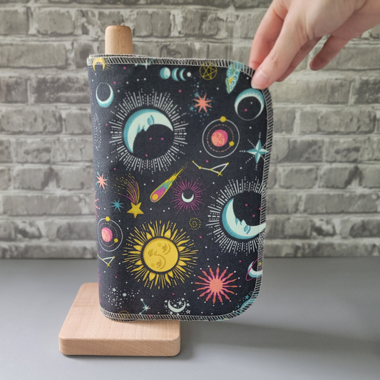 The gray celestial nonpaper towels on the same wooden holder, with my hand holding the top corner of the towel as if I'm pulling it off the roll. The corners of the towel are rounded and stitched in an off-white thread.
