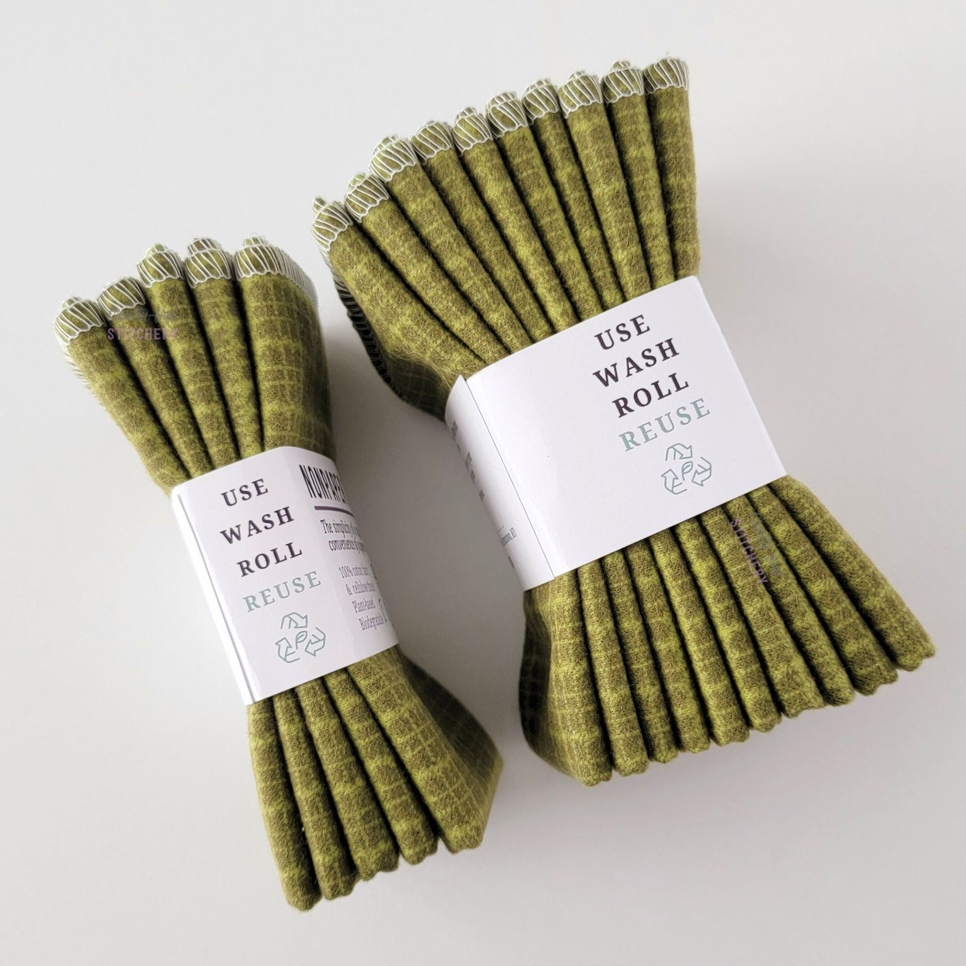 Two packages of the Green Kitchen Plaid NonPaper Towels, shown on their side so display the 5-pack and 10-packs. The side of the paper tag says "use, wash, roll, reuse" and has the recycling logo with a leaf in the center, to symbolize they are biodegradable.